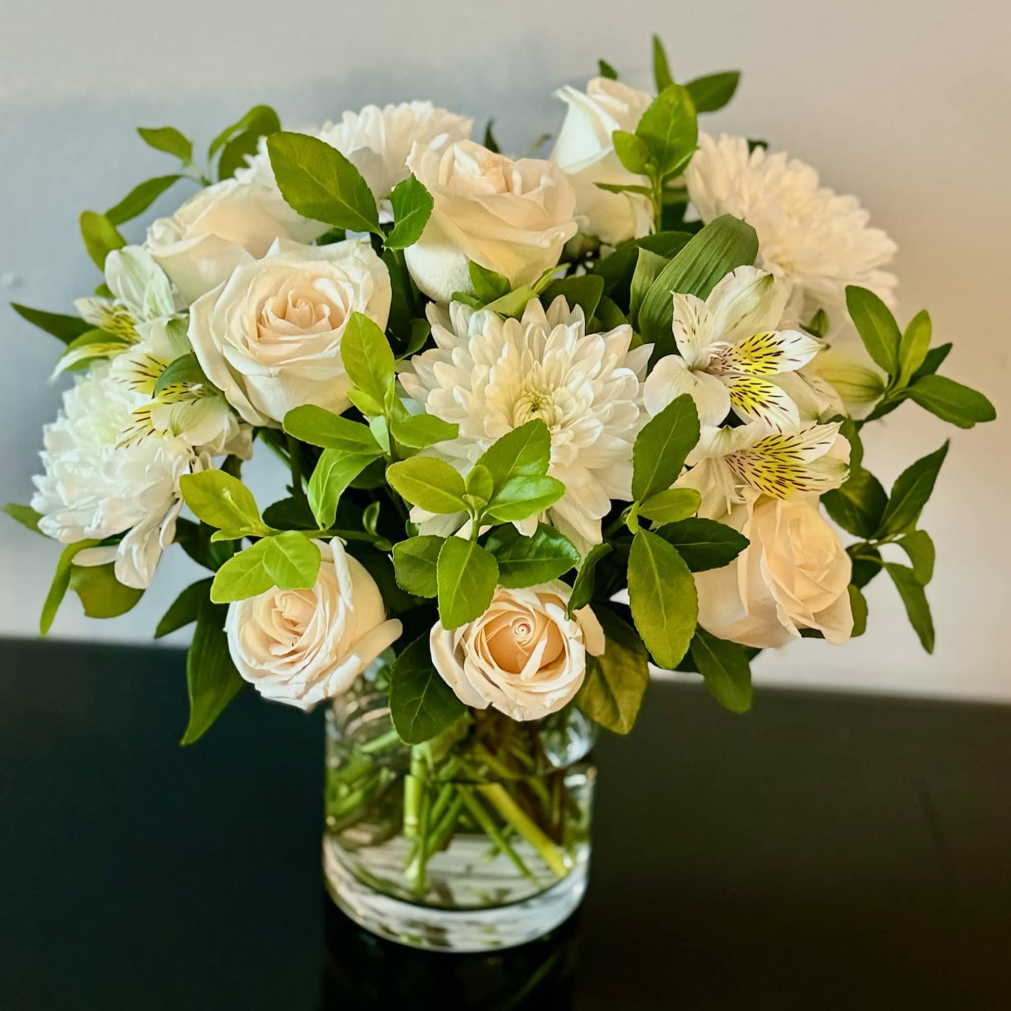 White roses and chrysanthemums in a clear glass vase with green foliage