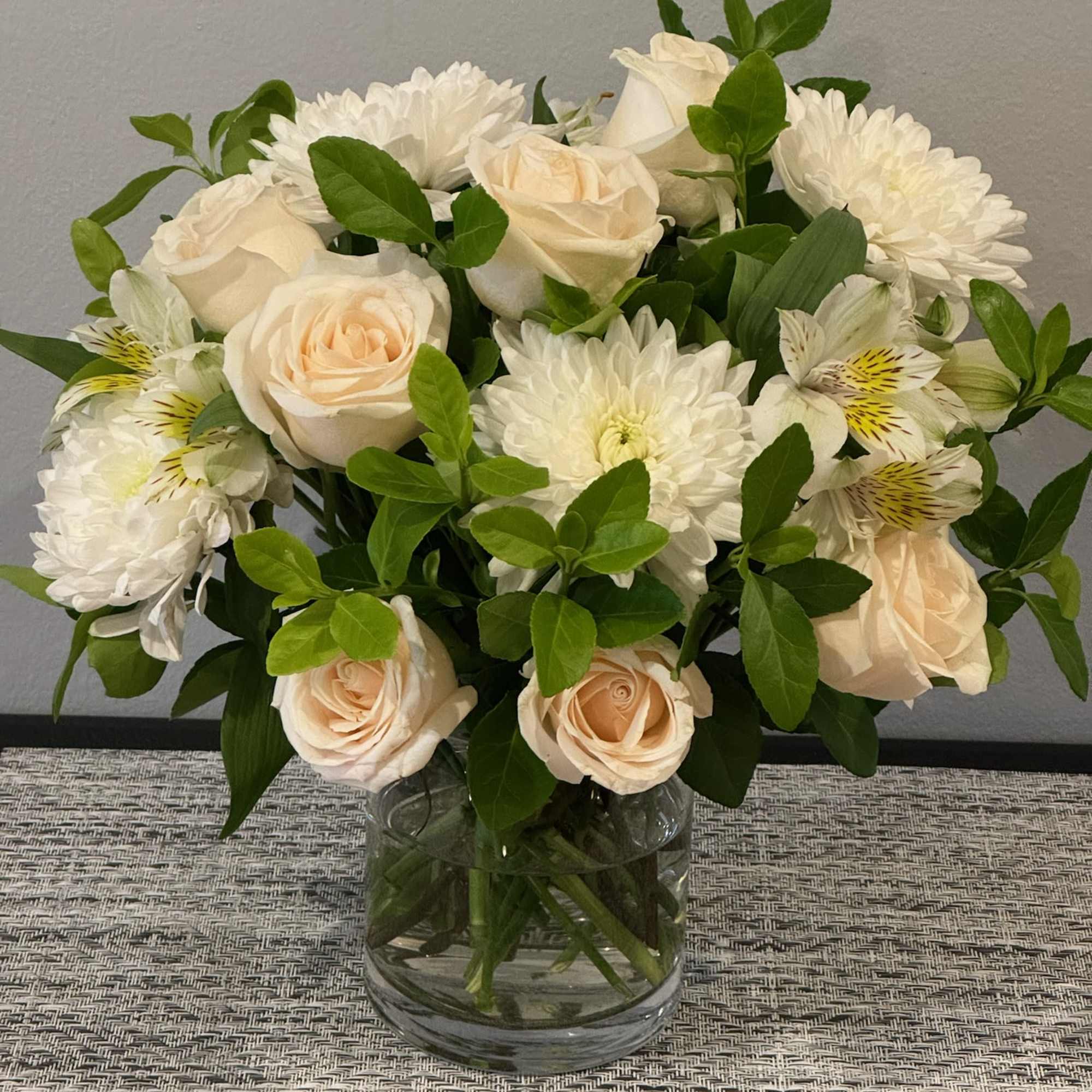 Cream roses and white daisies arranged in a clear glass vase
