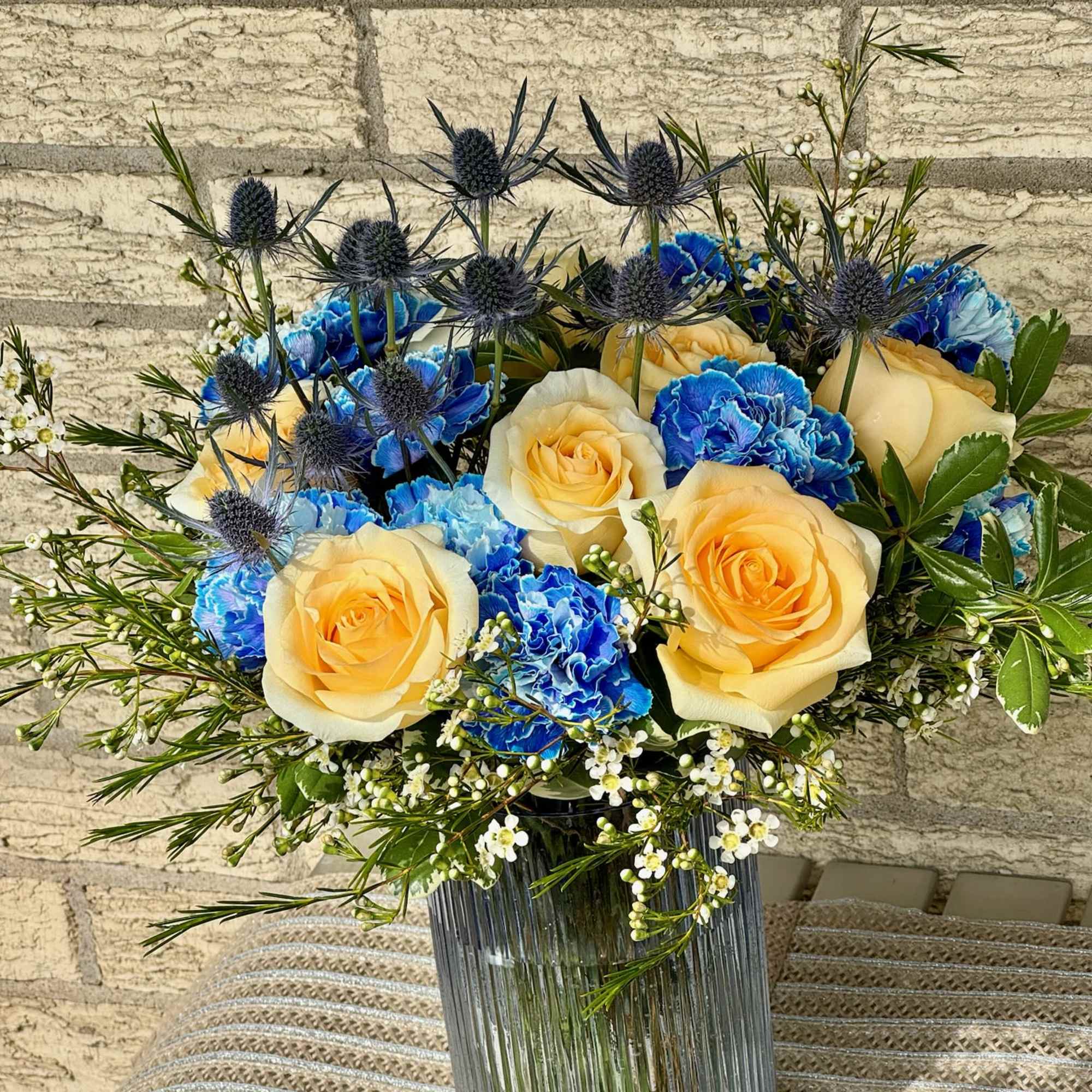 Yellow roses and blue carnations in a glass vase