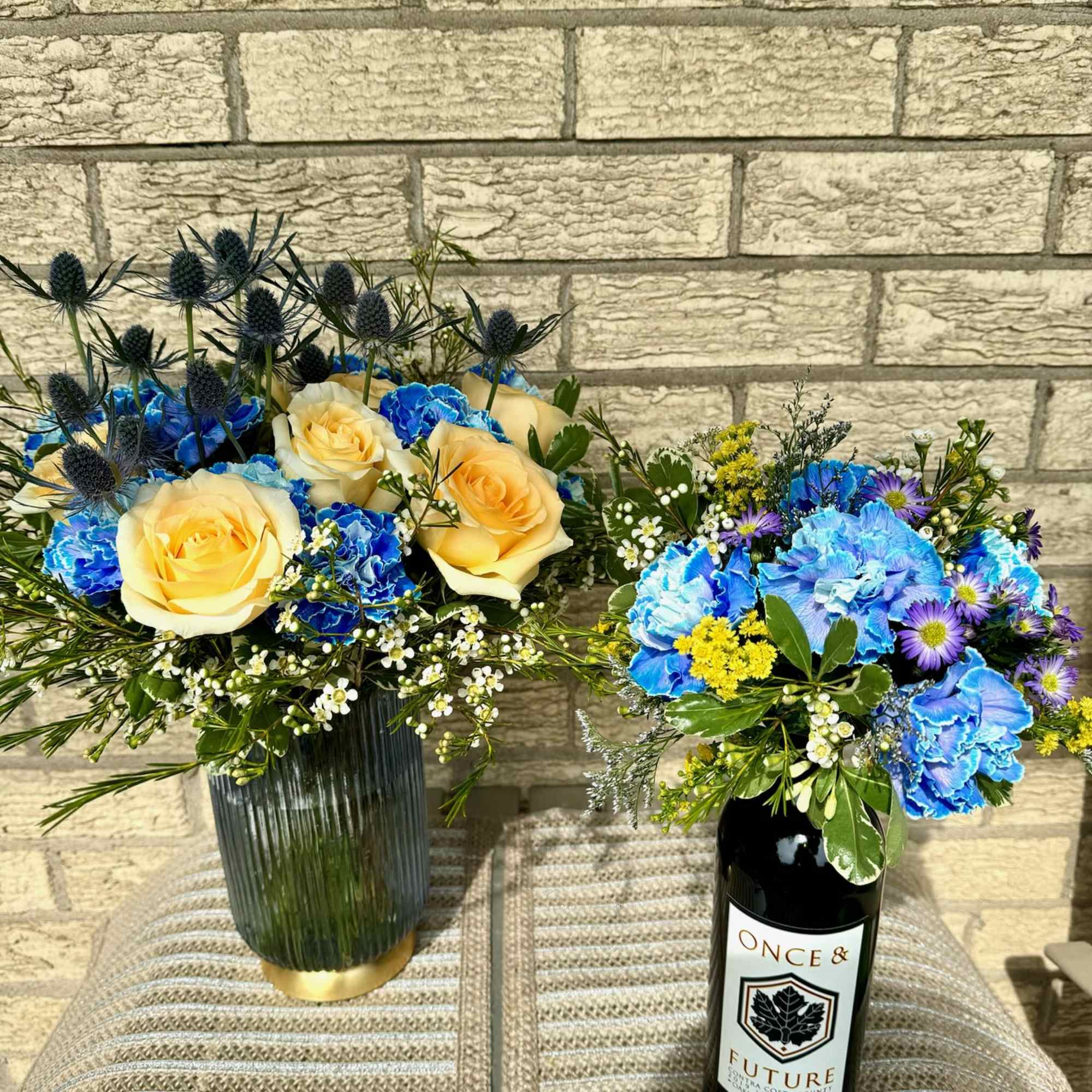 Two floral arrangements in vases, one beside a wine bottle