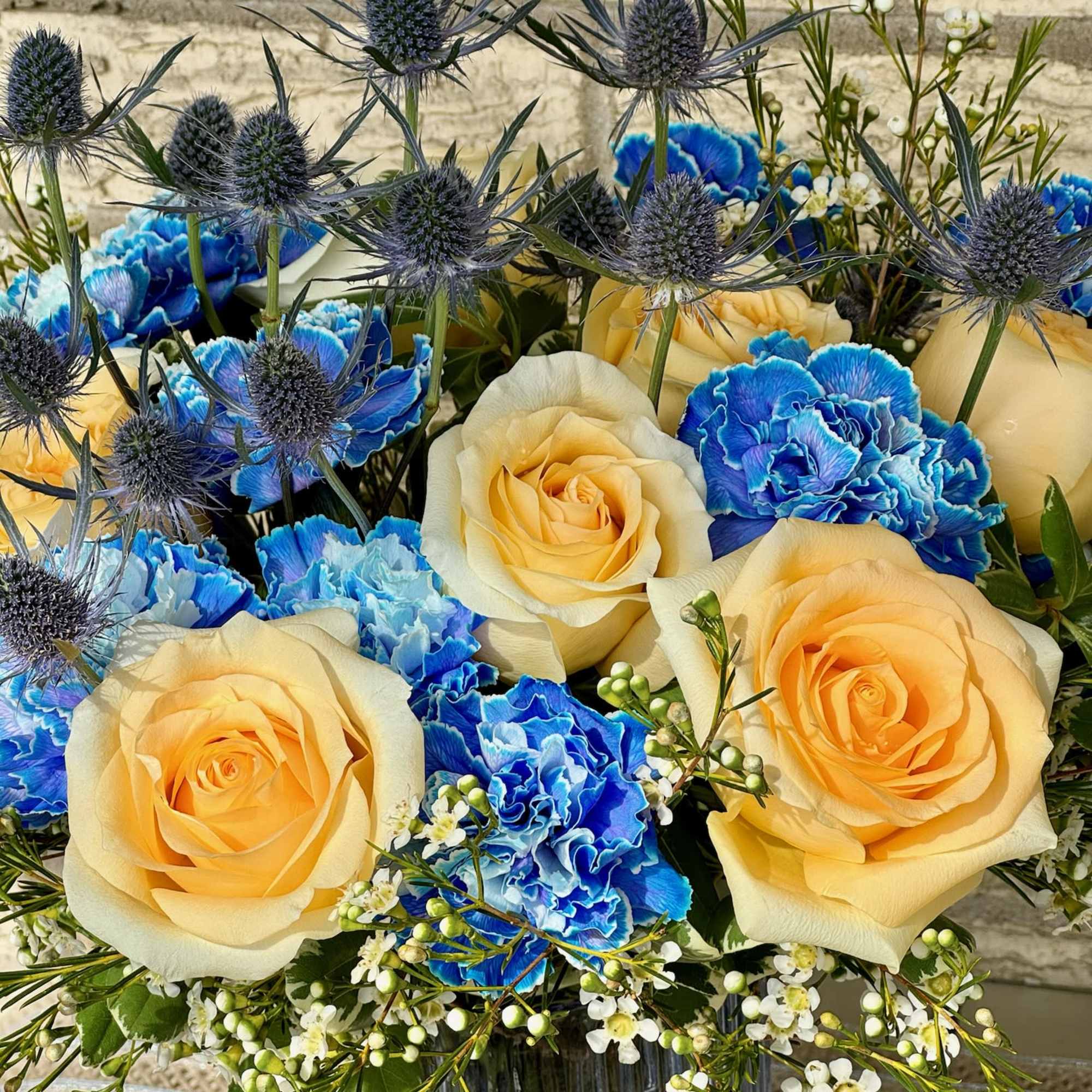 Bouquet of yellow roses, blue carnations, and thistle in a glass vase
