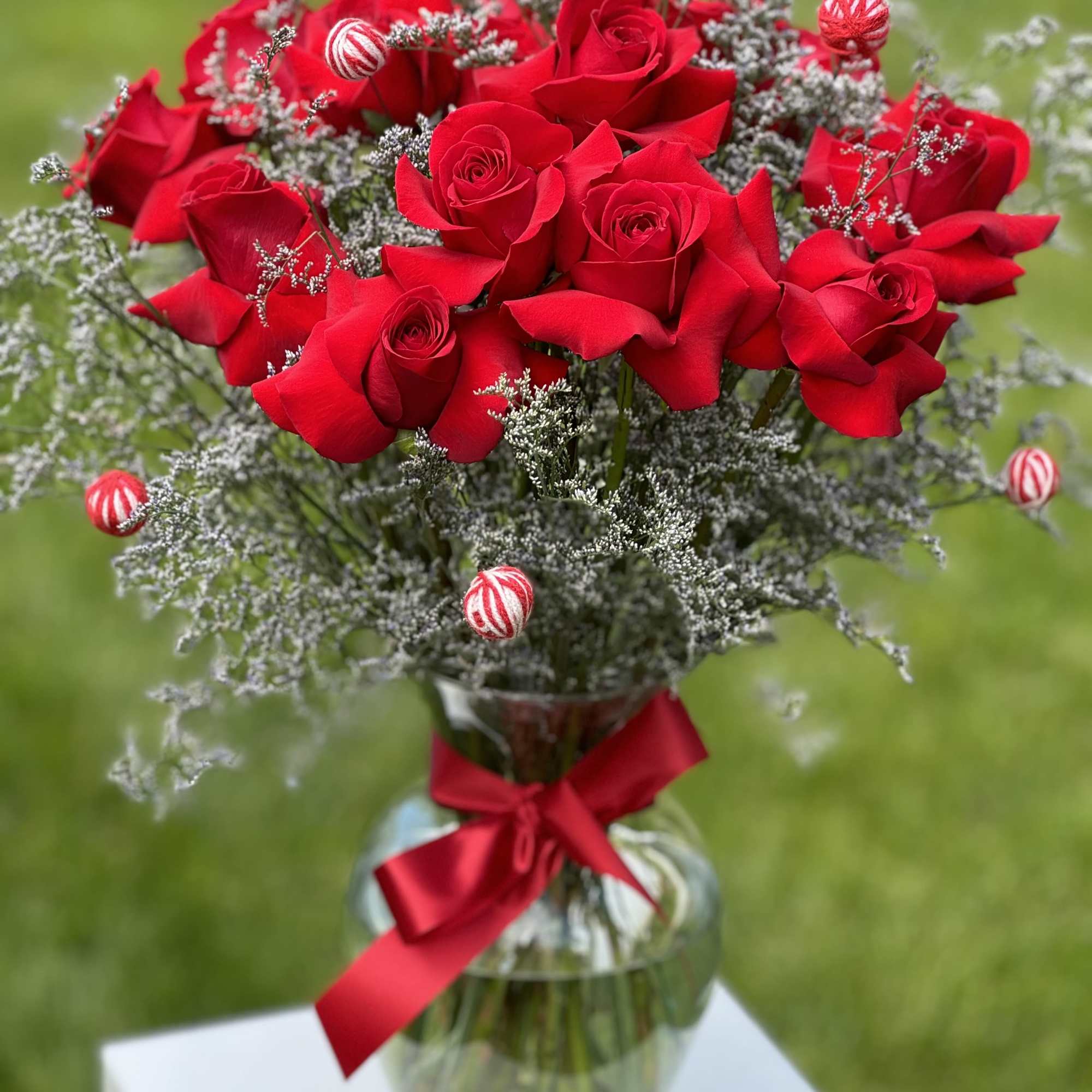 Red roses arranged in a glass vase with a red ribbon