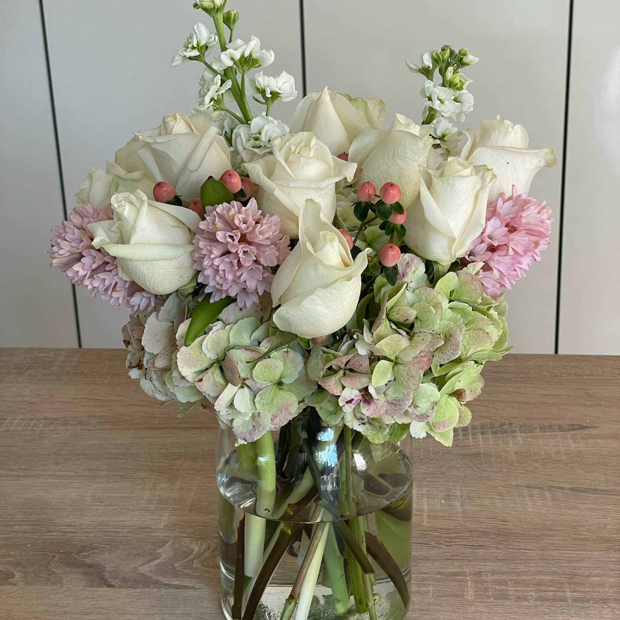 White roses and pale pink blooms arranged in a clear glass vase
