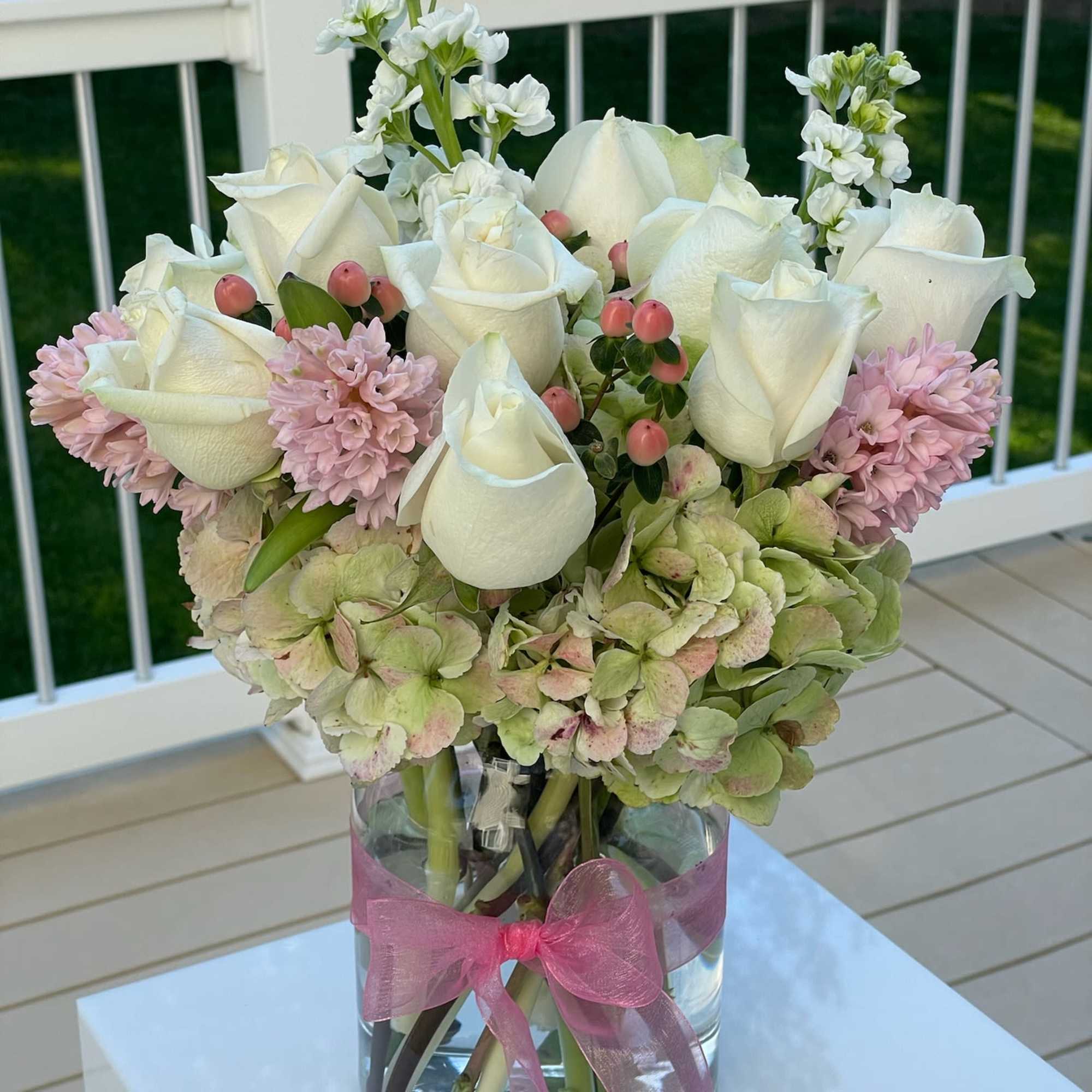 White roses and pink flowers arranged in a glass vase with a pink ribbon