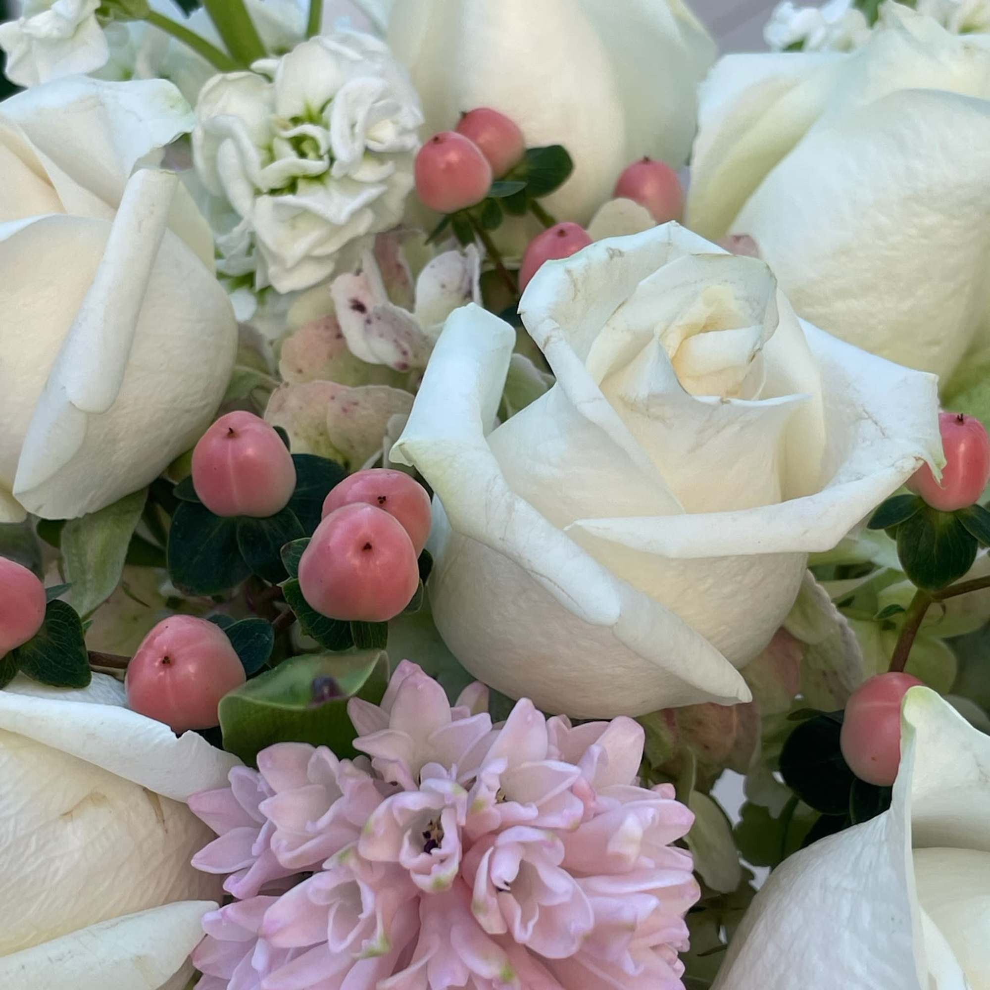 White roses and pale pink flowers with pink berries in a close-up bouquet