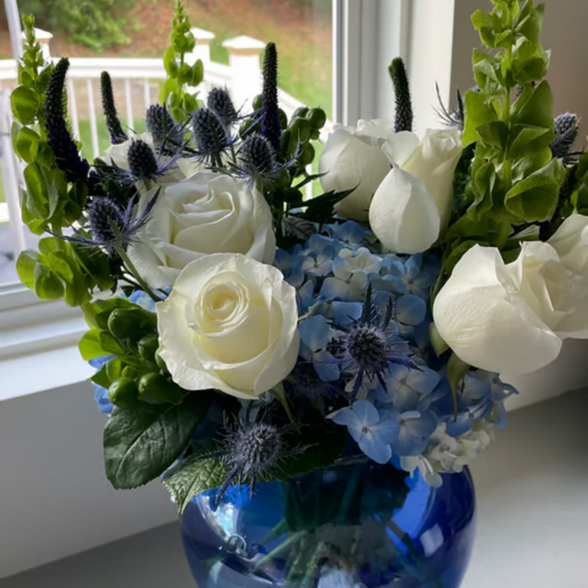White roses and blue hydrangeas in a blue glass vase