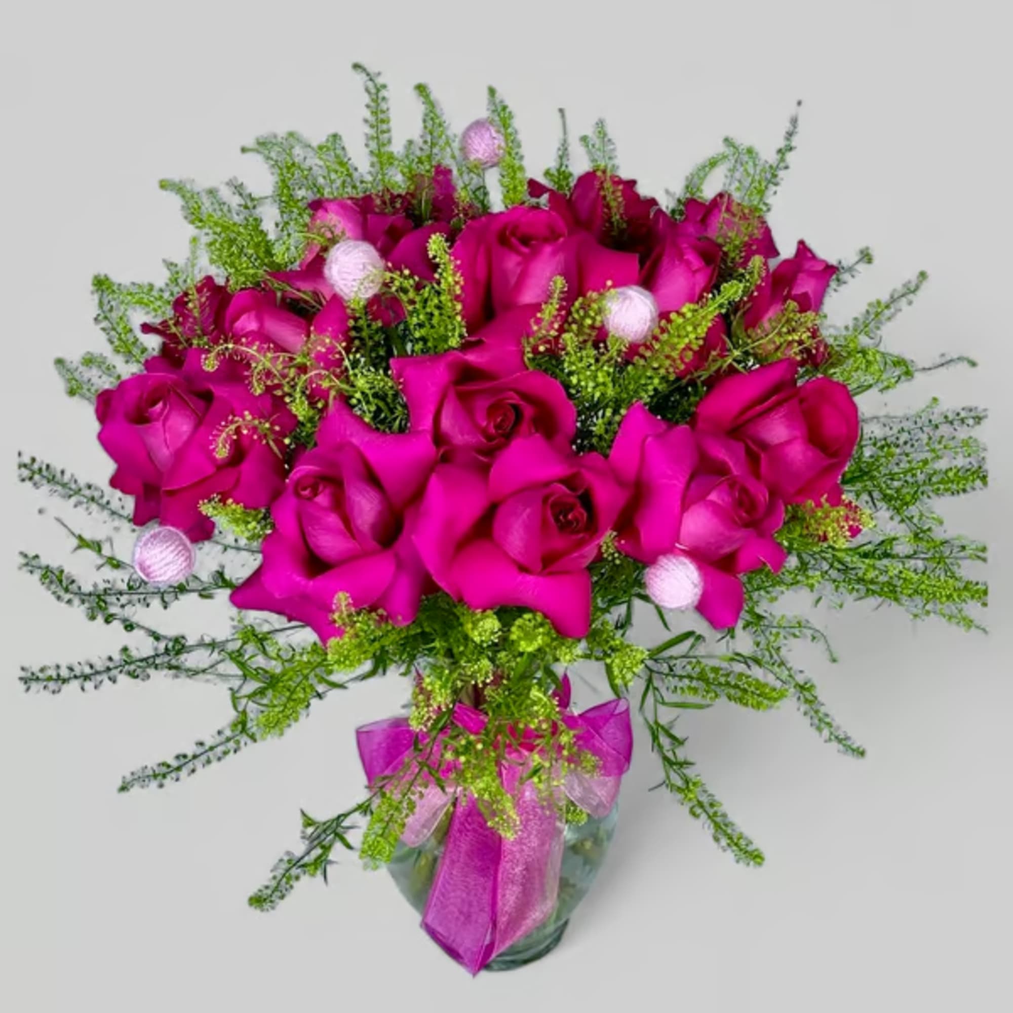 Bouquet of bright pink roses in a glass vase with green filler and ribbon