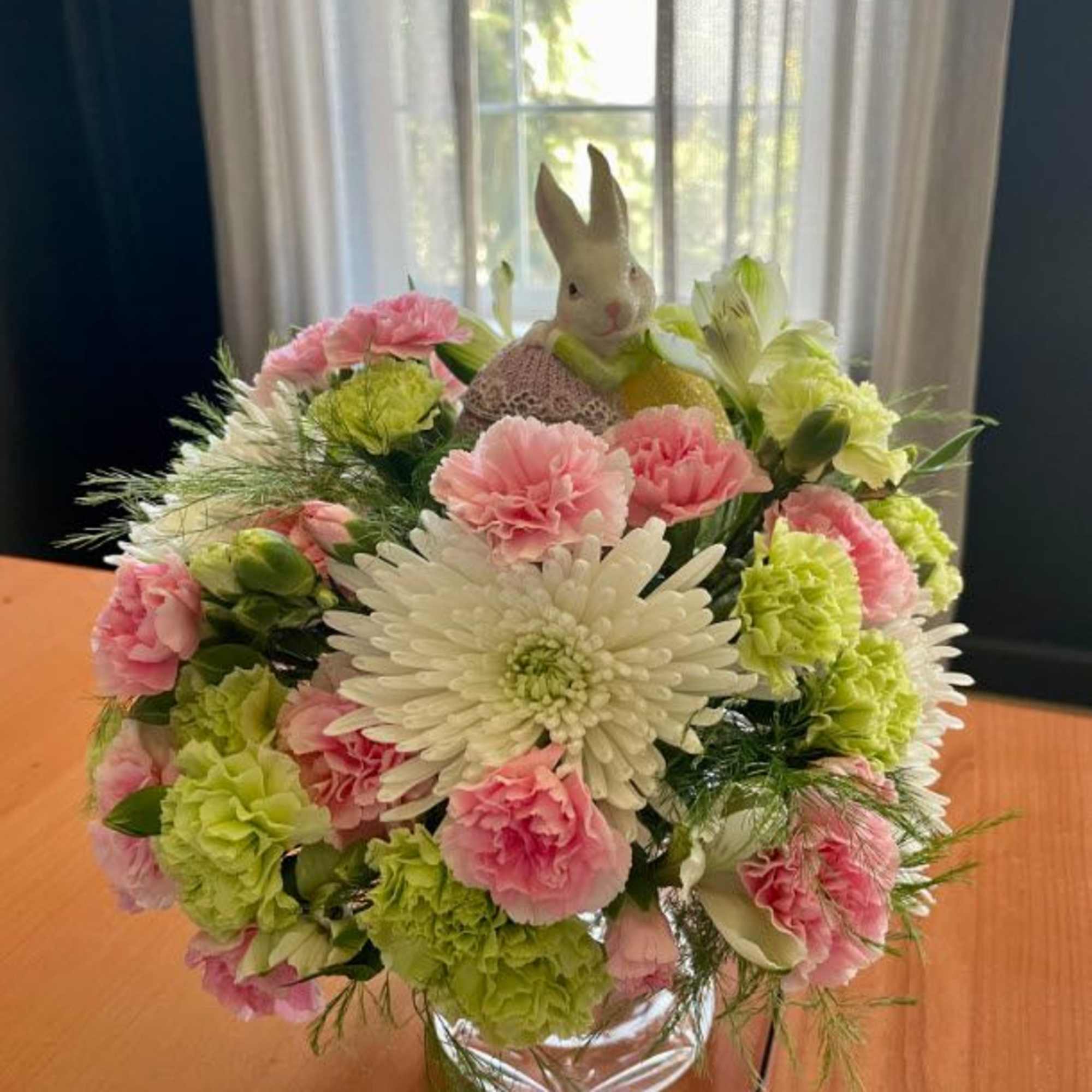 Bouquet of pink and green flowers in a glass vase with a small bunny figurine