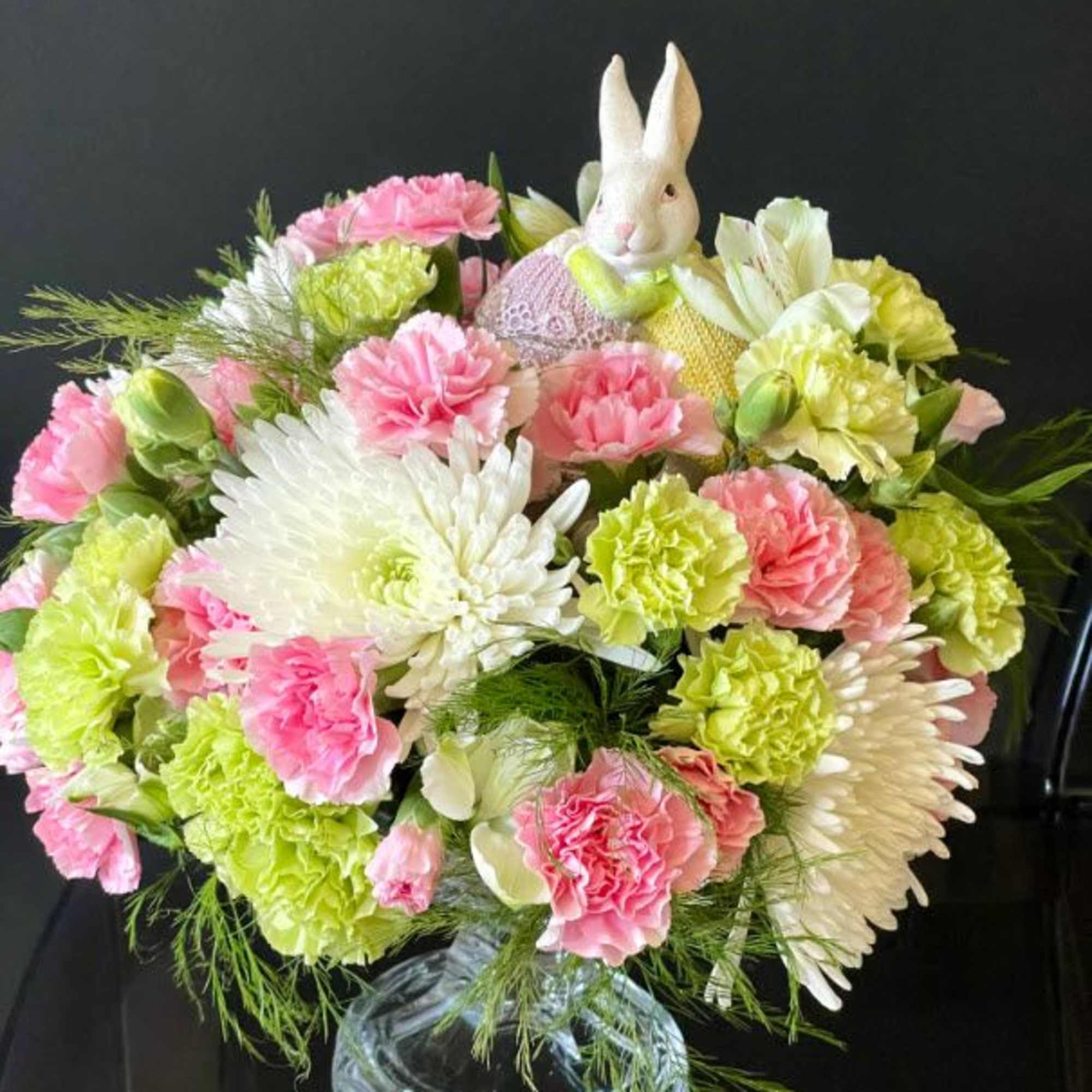 Pink and green flower arrangement in a glass vase with a small bunny figurine