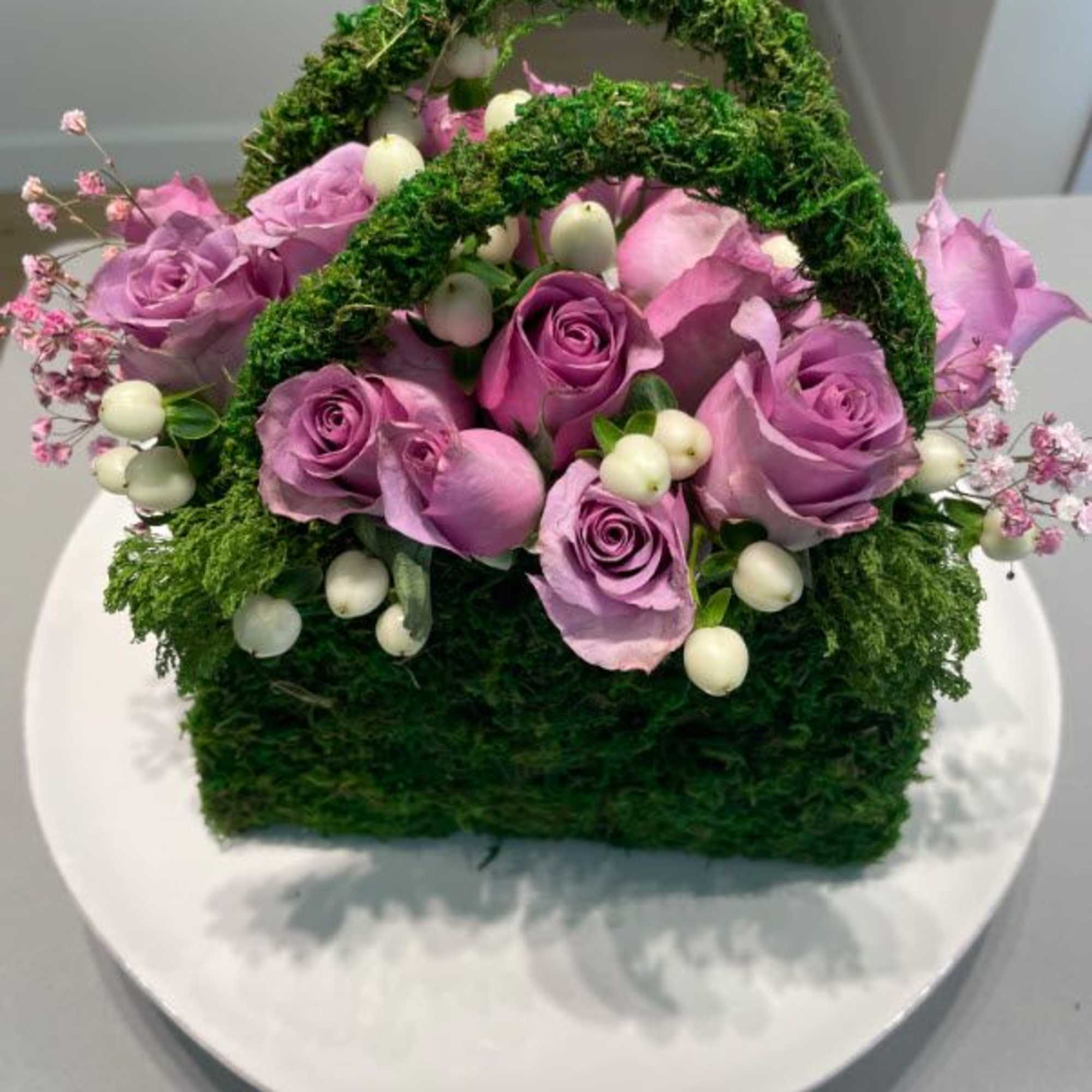 Basket arrangement of lavender roses with white berries and moss handles