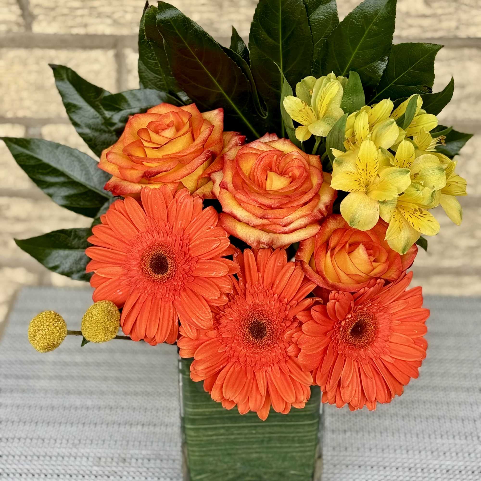 Orange roses and gerbera daisies in a square glass vase