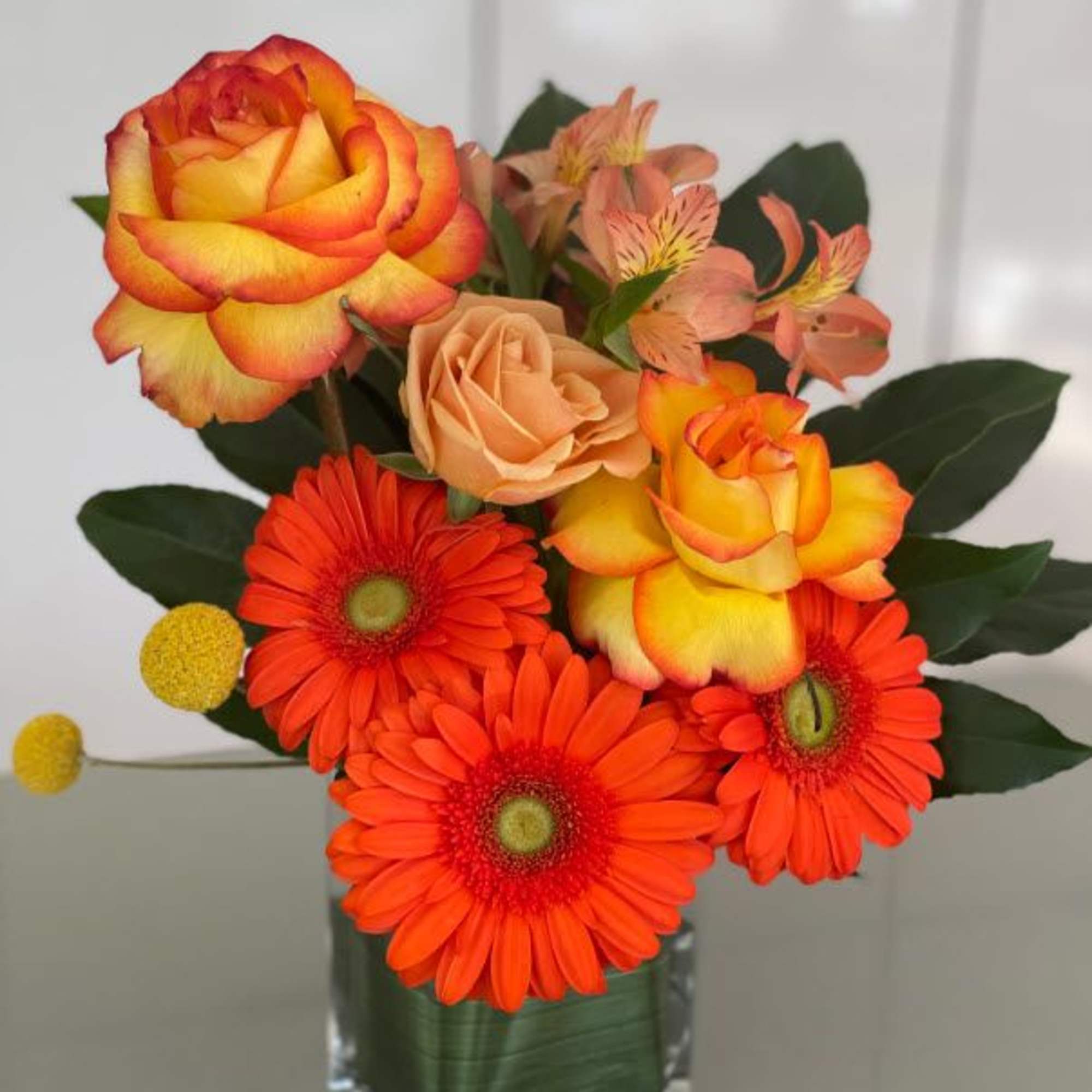 Orange and yellow roses with bright orange gerbera daisies in a glass vase