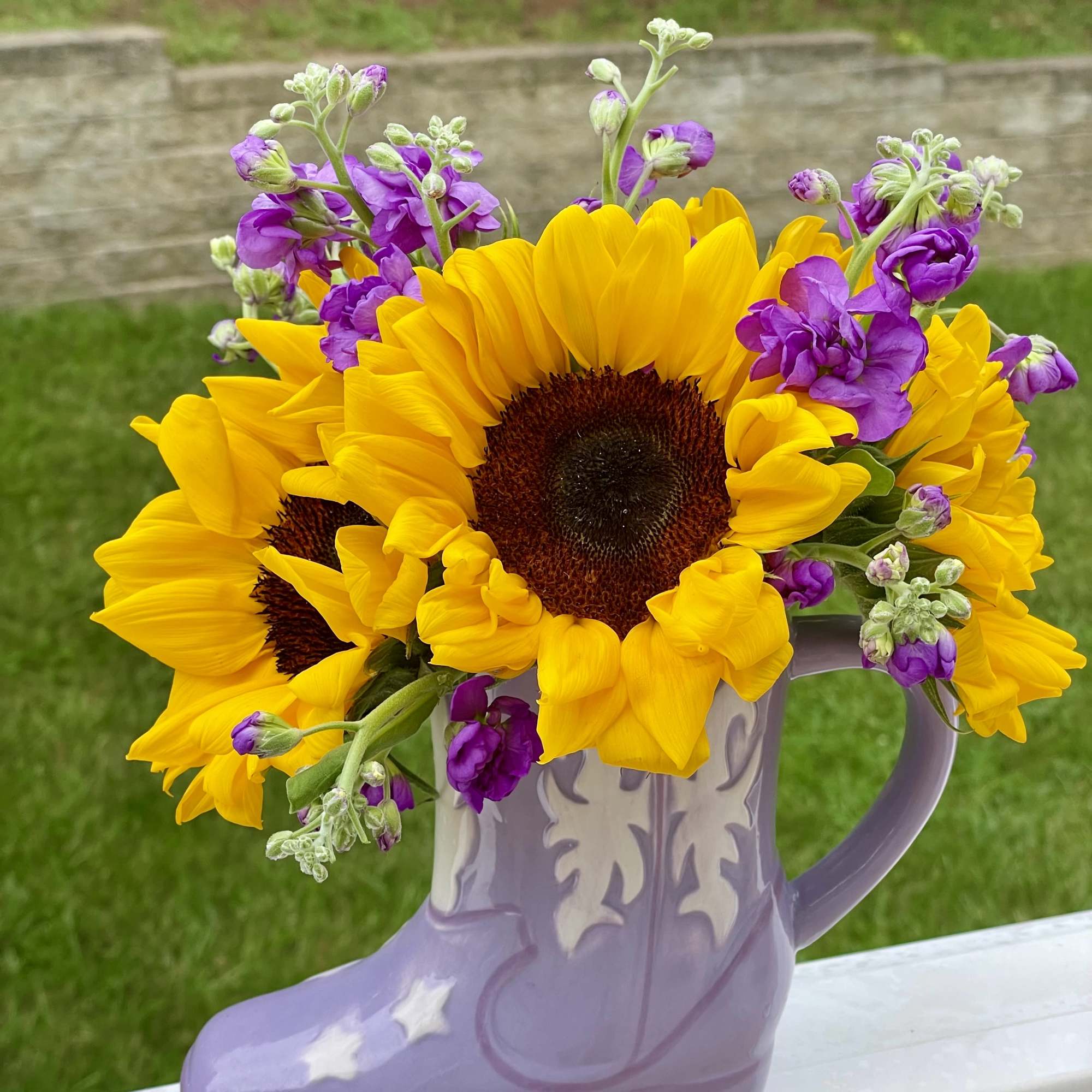 Sunflowers and purple flowers arranged in a lavender boot-shaped vase