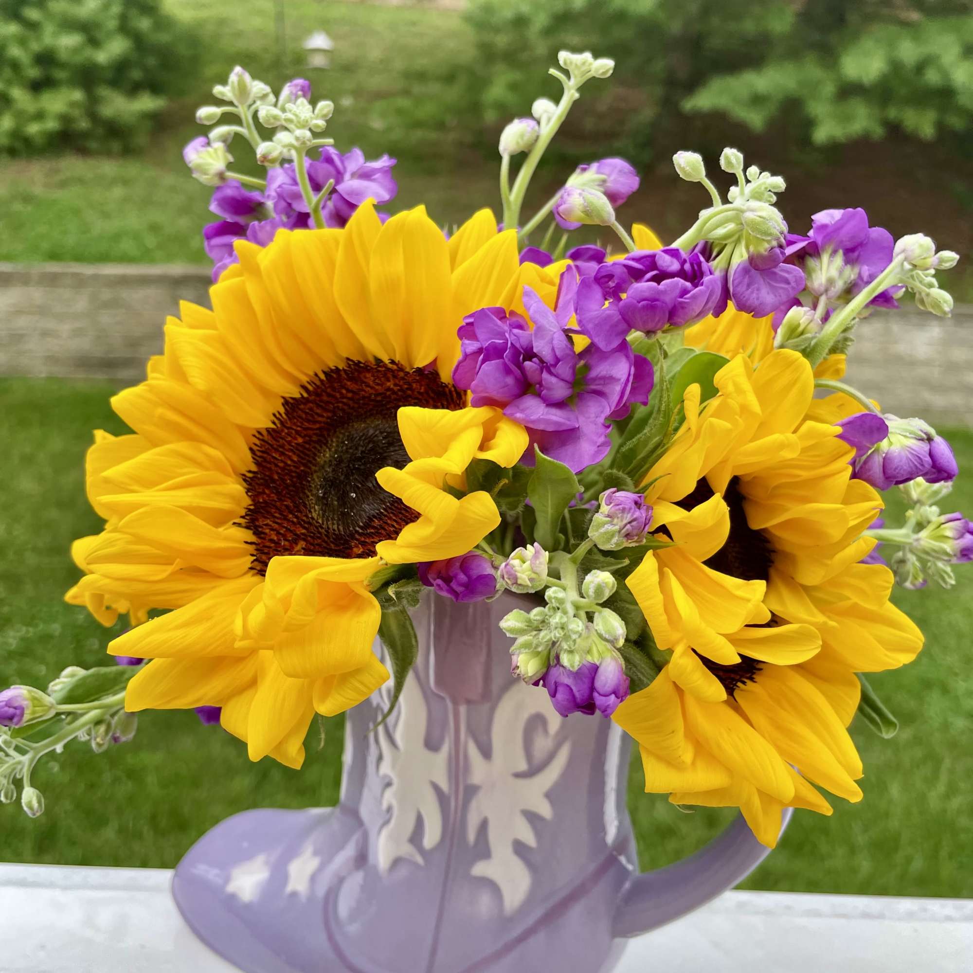 Sunflowers and purple flowers in a lavender pitcher vase