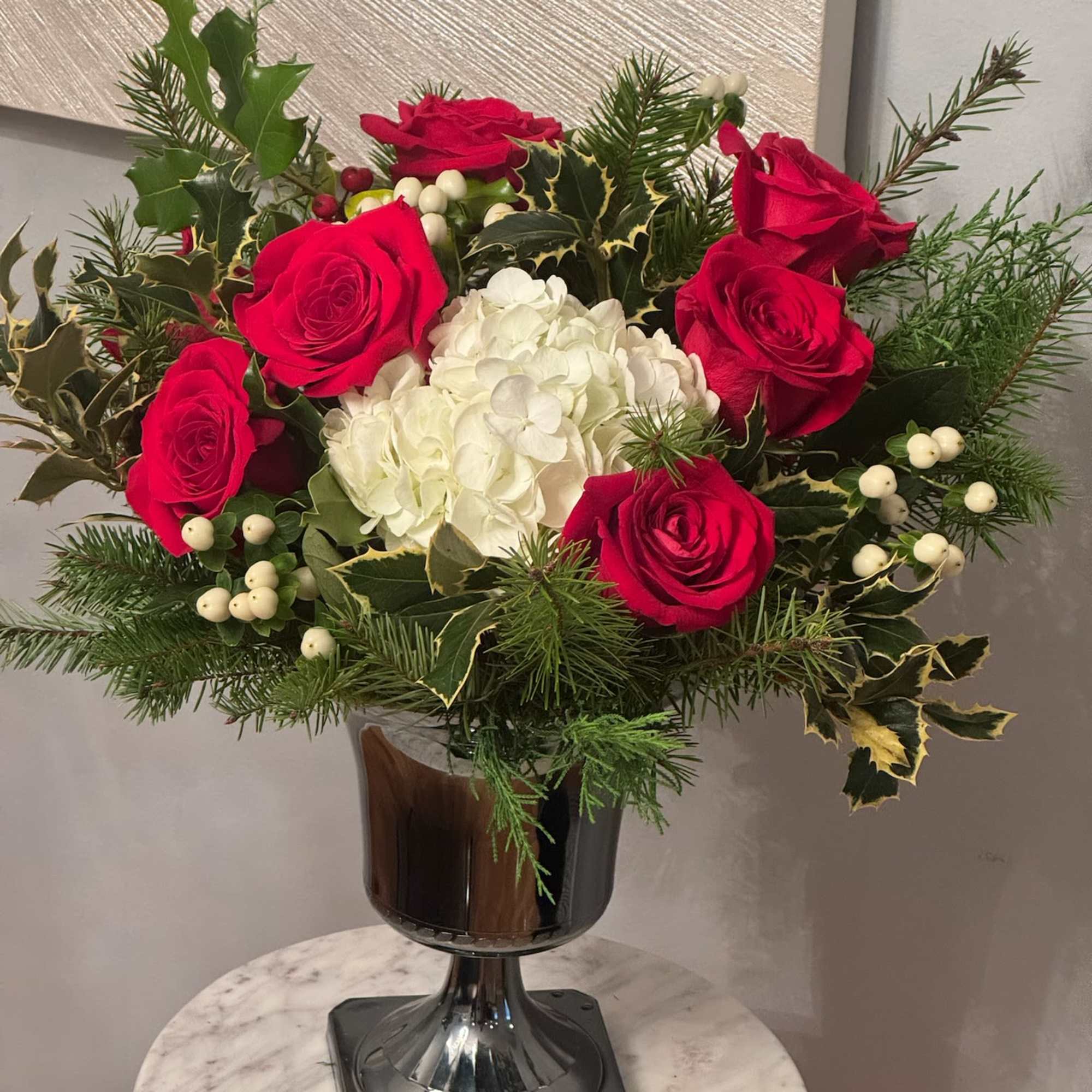 Red roses and white hydrangea in a glass vase with winter greenery