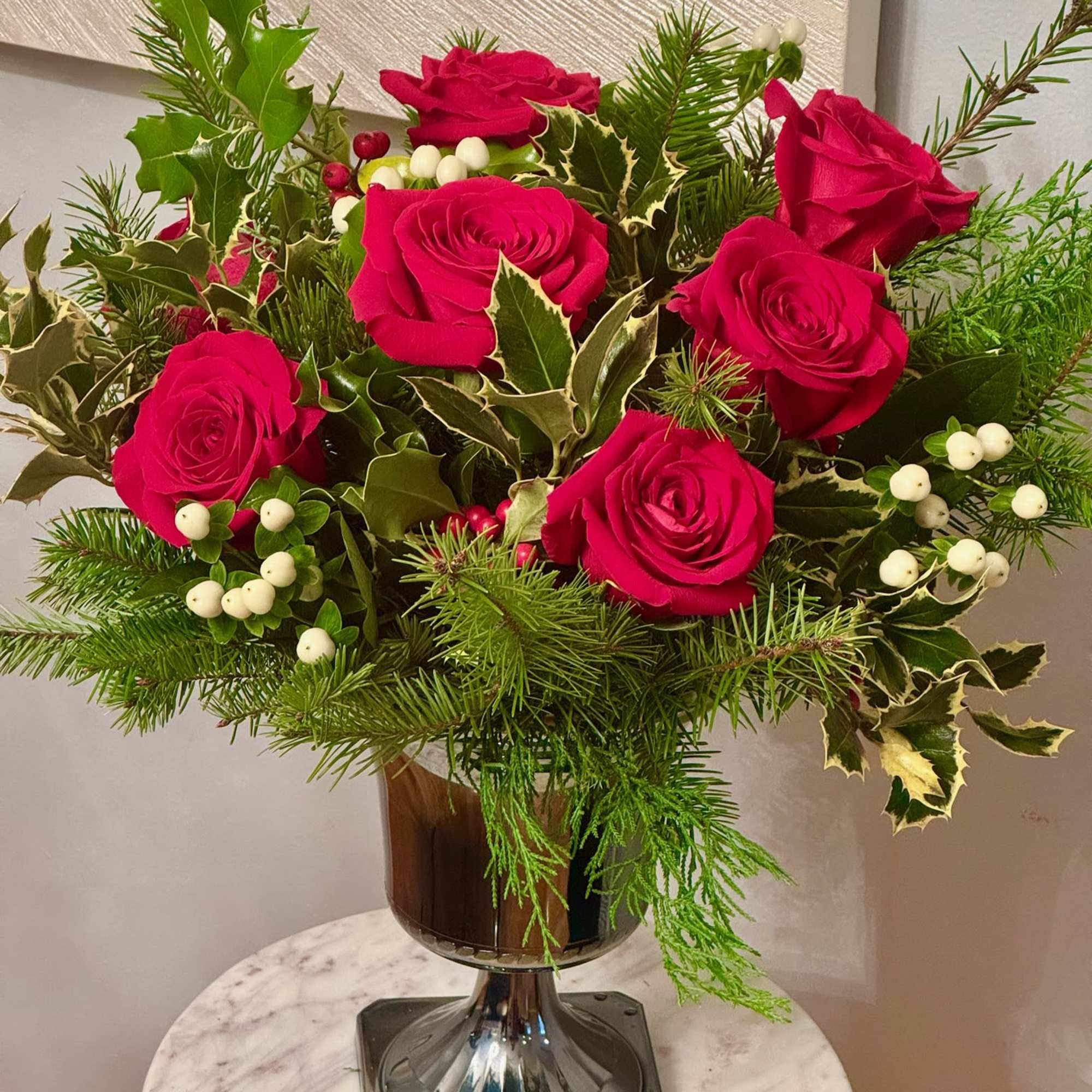 Red roses arranged in a glass vase with evergreen and white berries