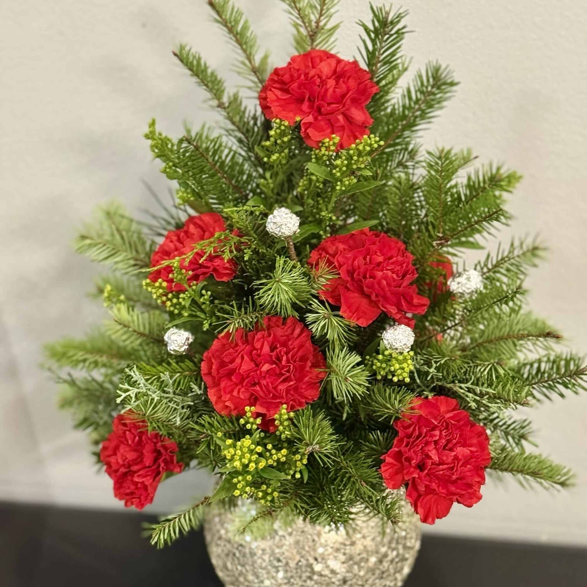 Red carnations in a glittery round vase with evergreen sprigs