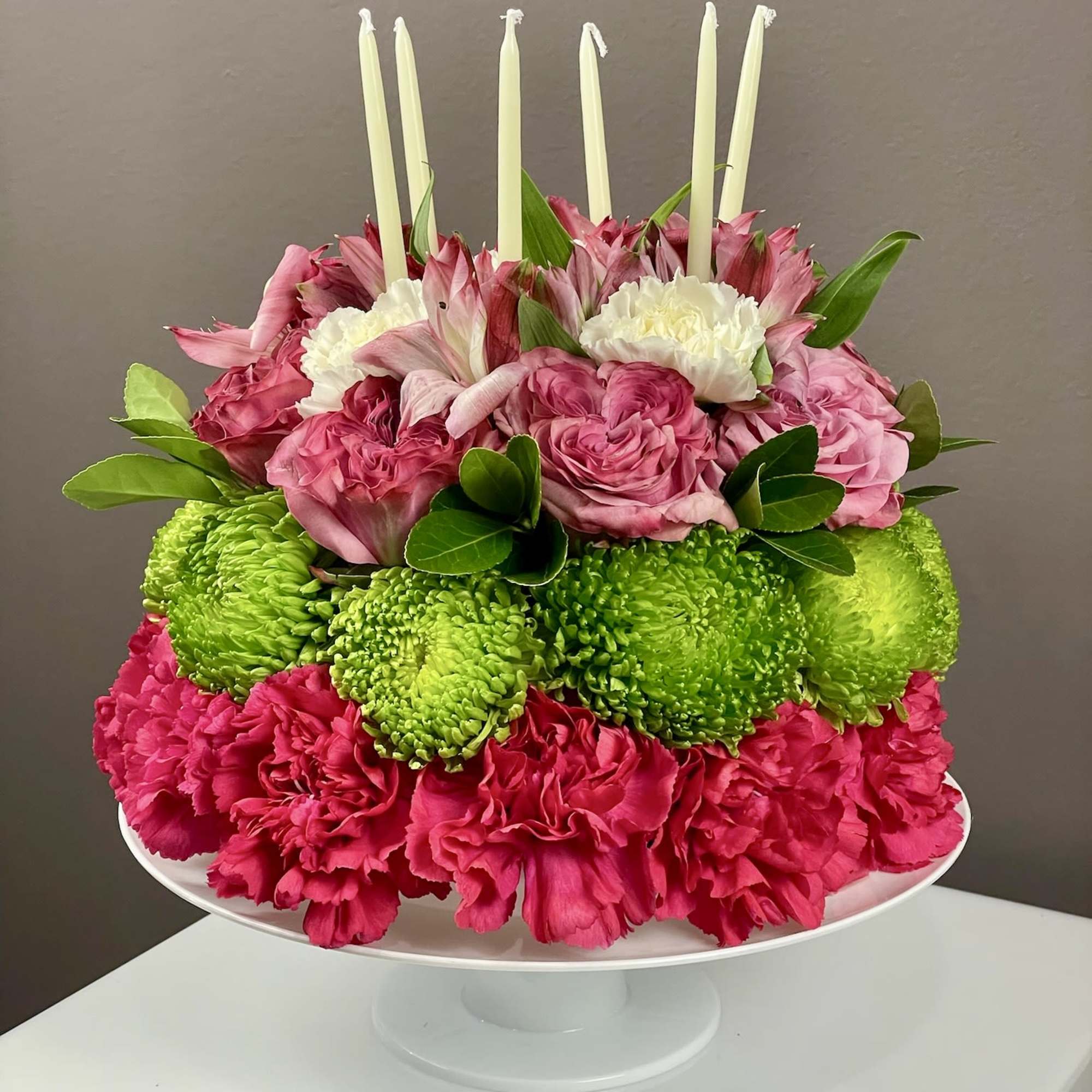 Pink and green floral centerpiece with white candles on a pedestal stand