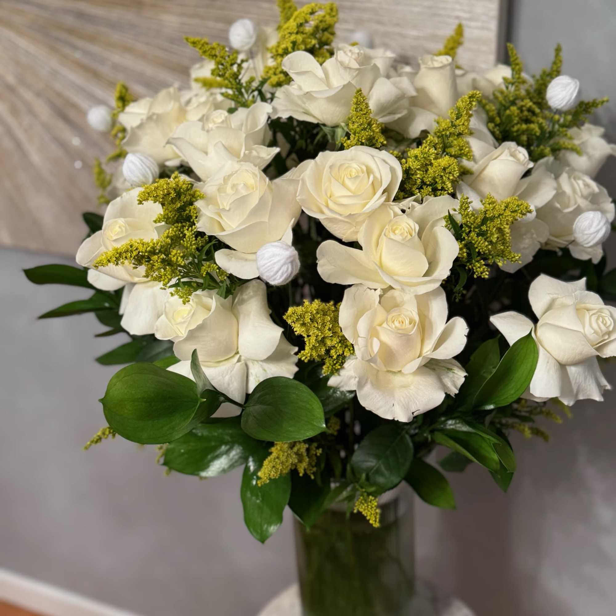 White roses arranged in a glass vase with yellow filler flowers