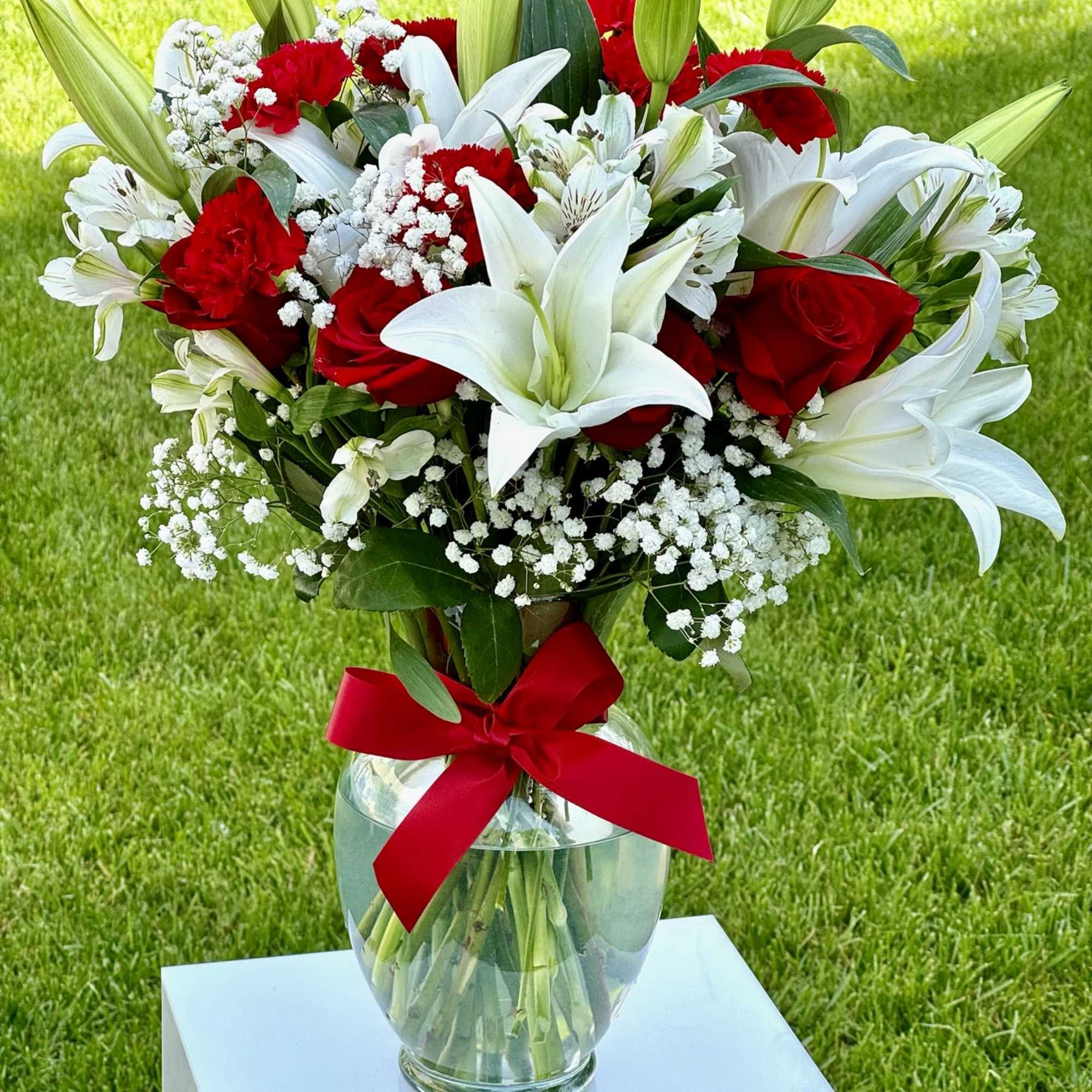 Bouquet of red roses and white lilies in a glass vase with a red ribbon