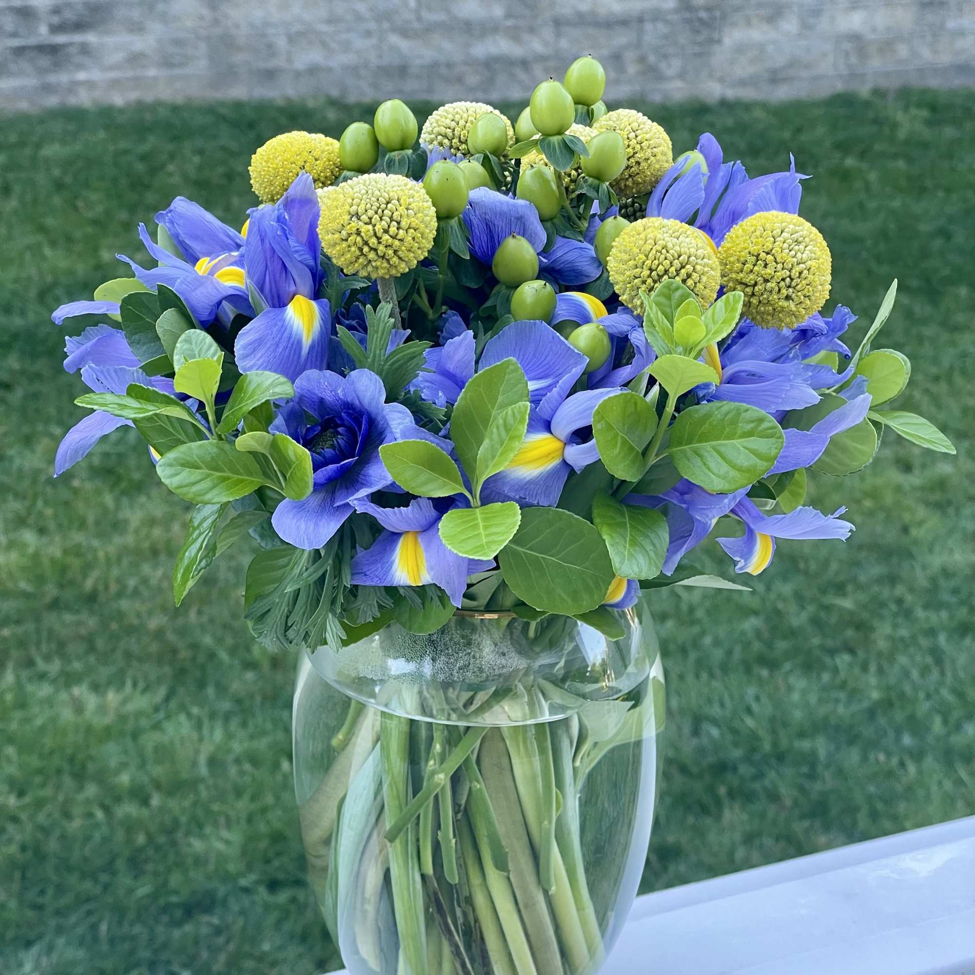 This vibrant arrangement features rich blue irises, sunny yellow billy balls, and, photo 3 of 3