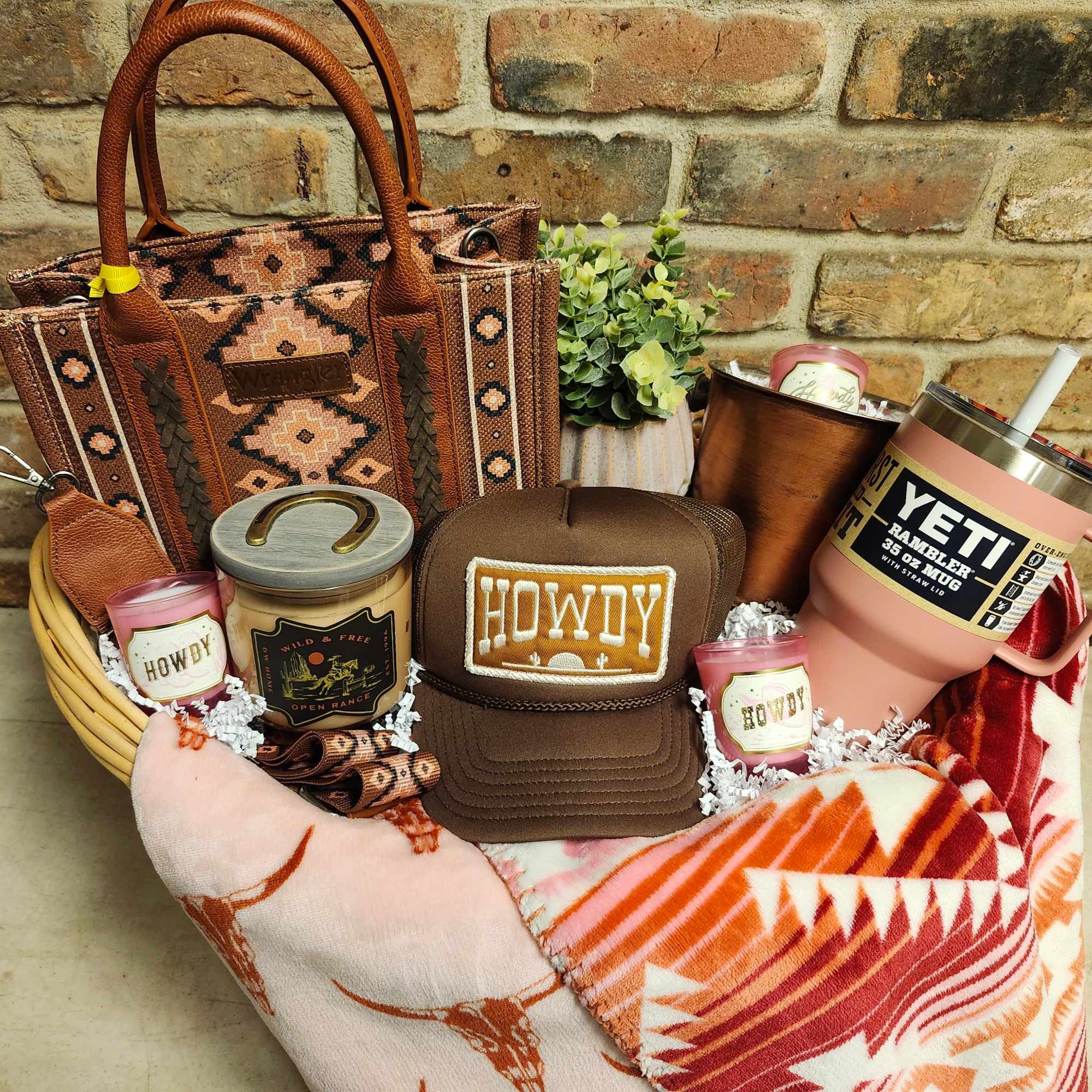 Gift basket with candles, a cap, tumbler, blanket, and a small plant