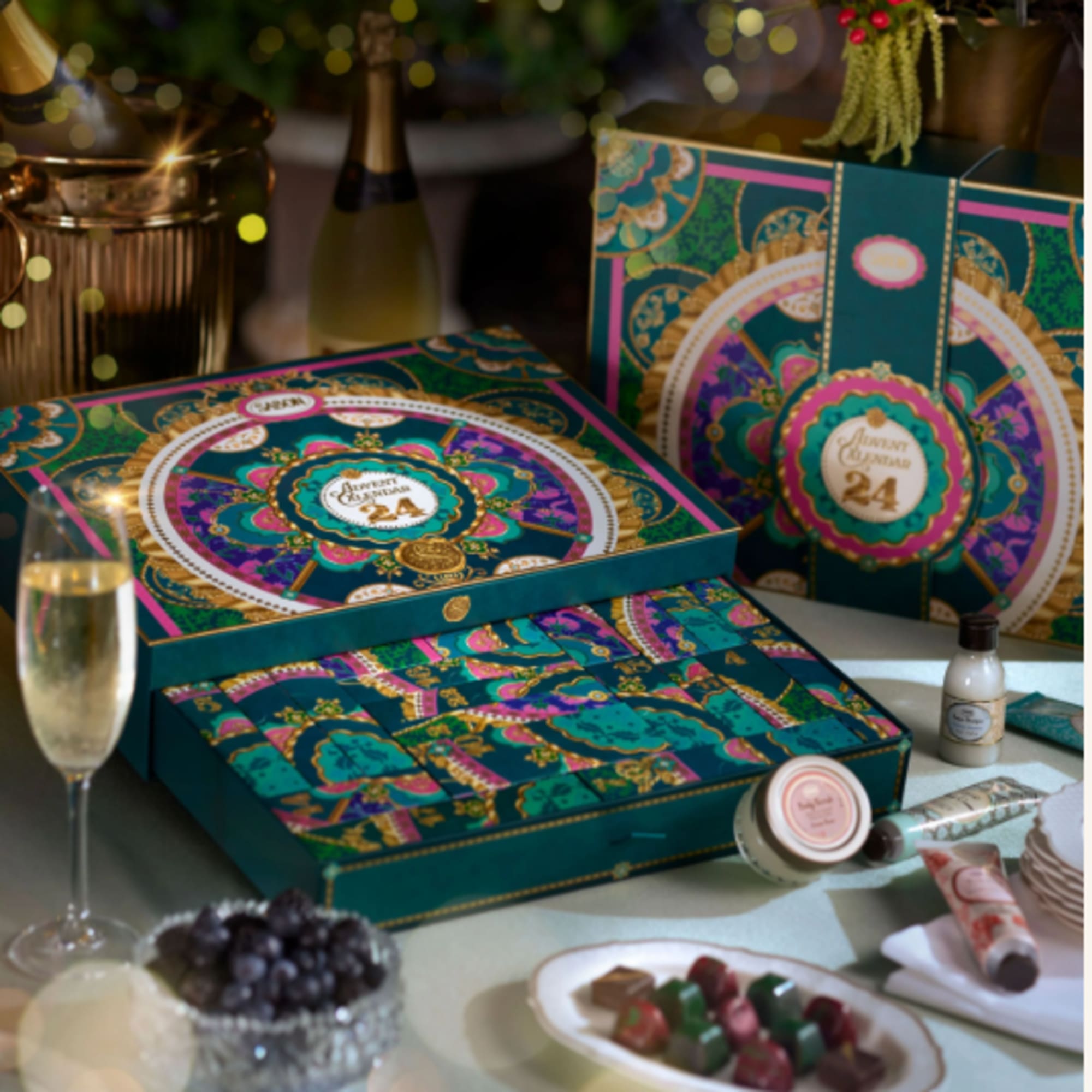 Gift boxes with ornate teal and gold patterns beside champagne and sweets