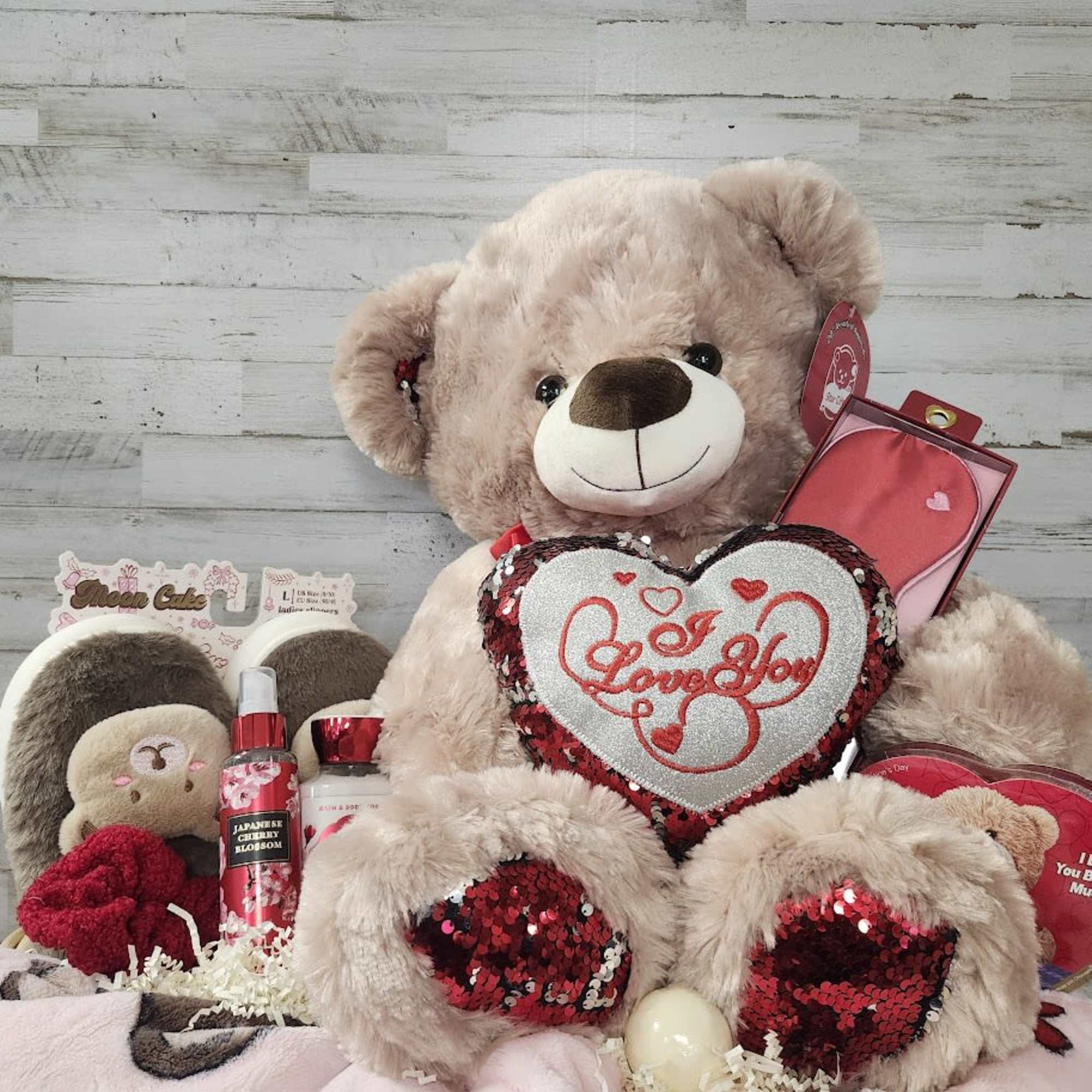 Large teddy bear holding a heart pillow with assorted gift items