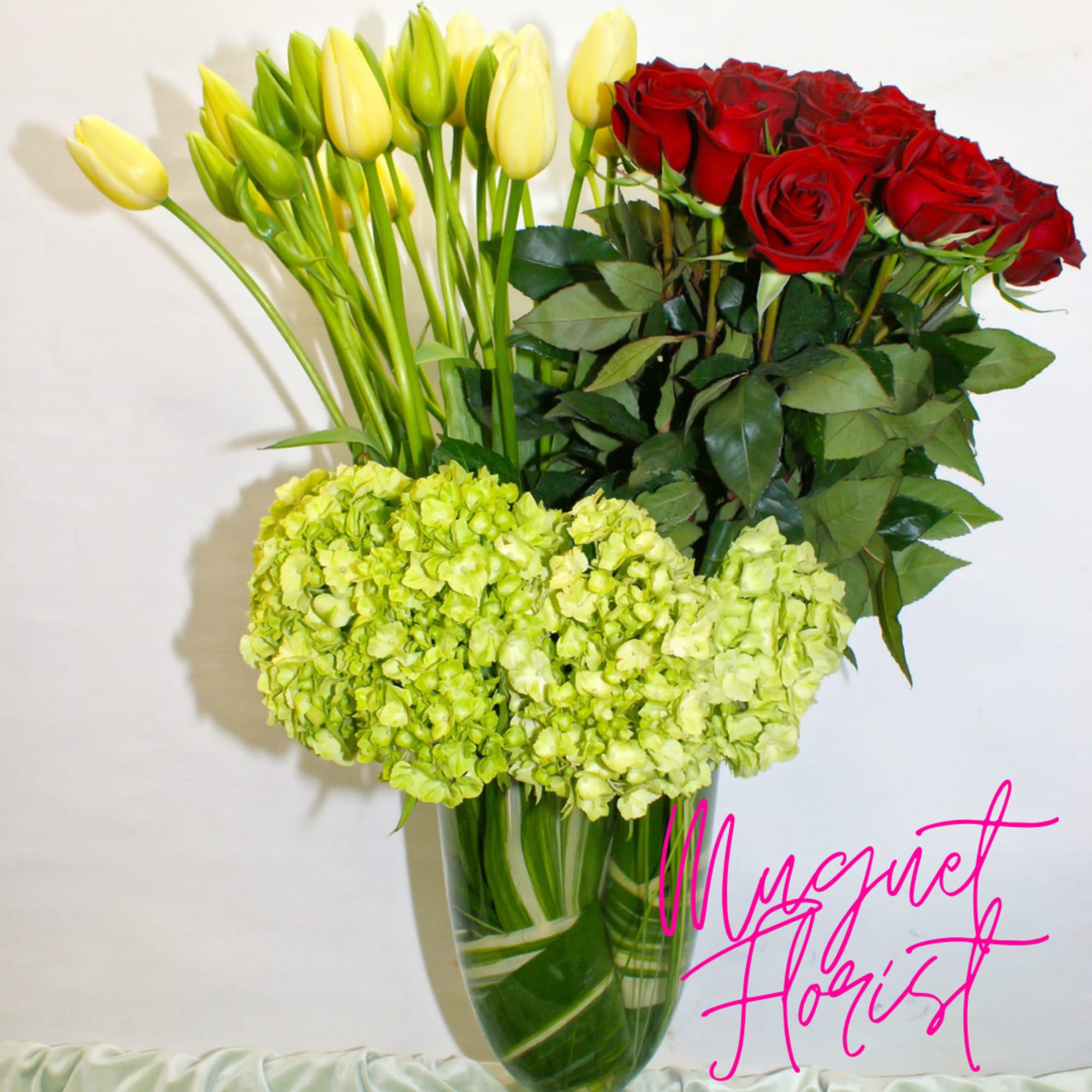 Bouquet of red roses, yellow tulips, and green hydrangeas in a glass vase
