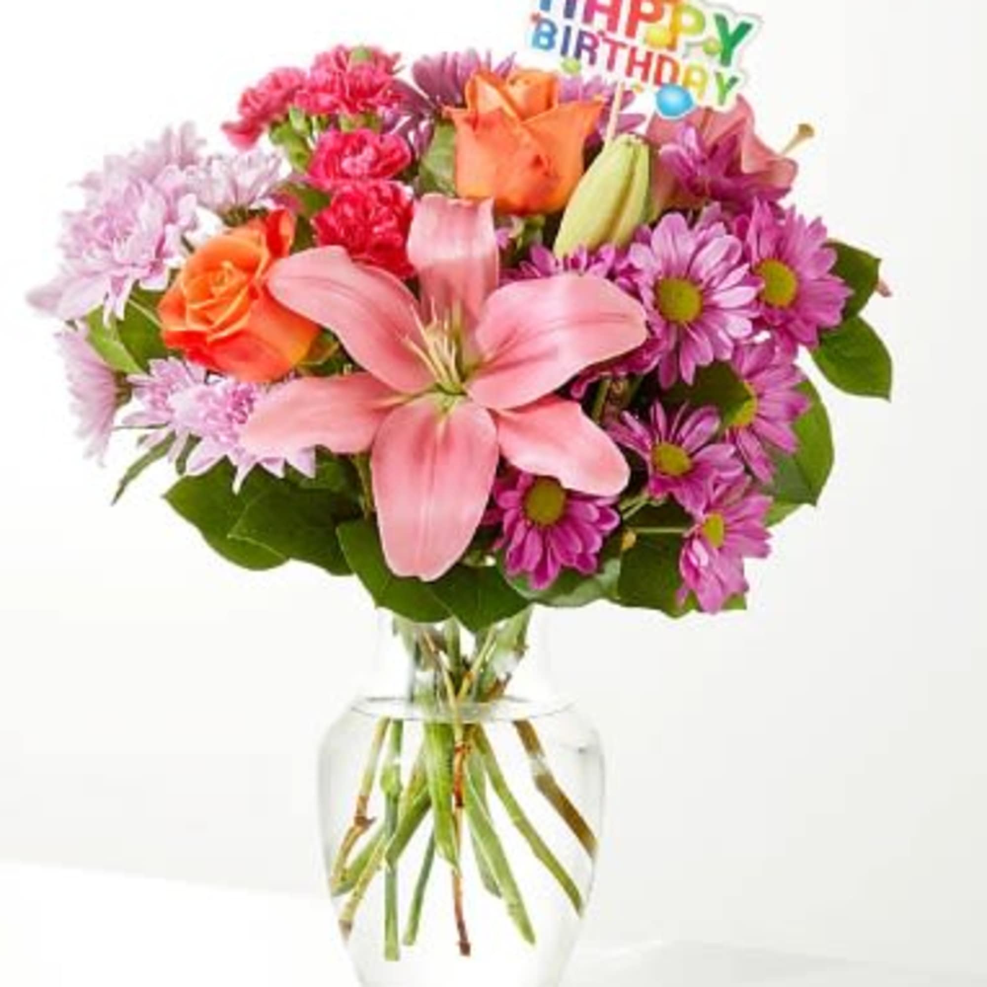 Mixed pink and orange flowers in a clear glass vase with a birthday topper