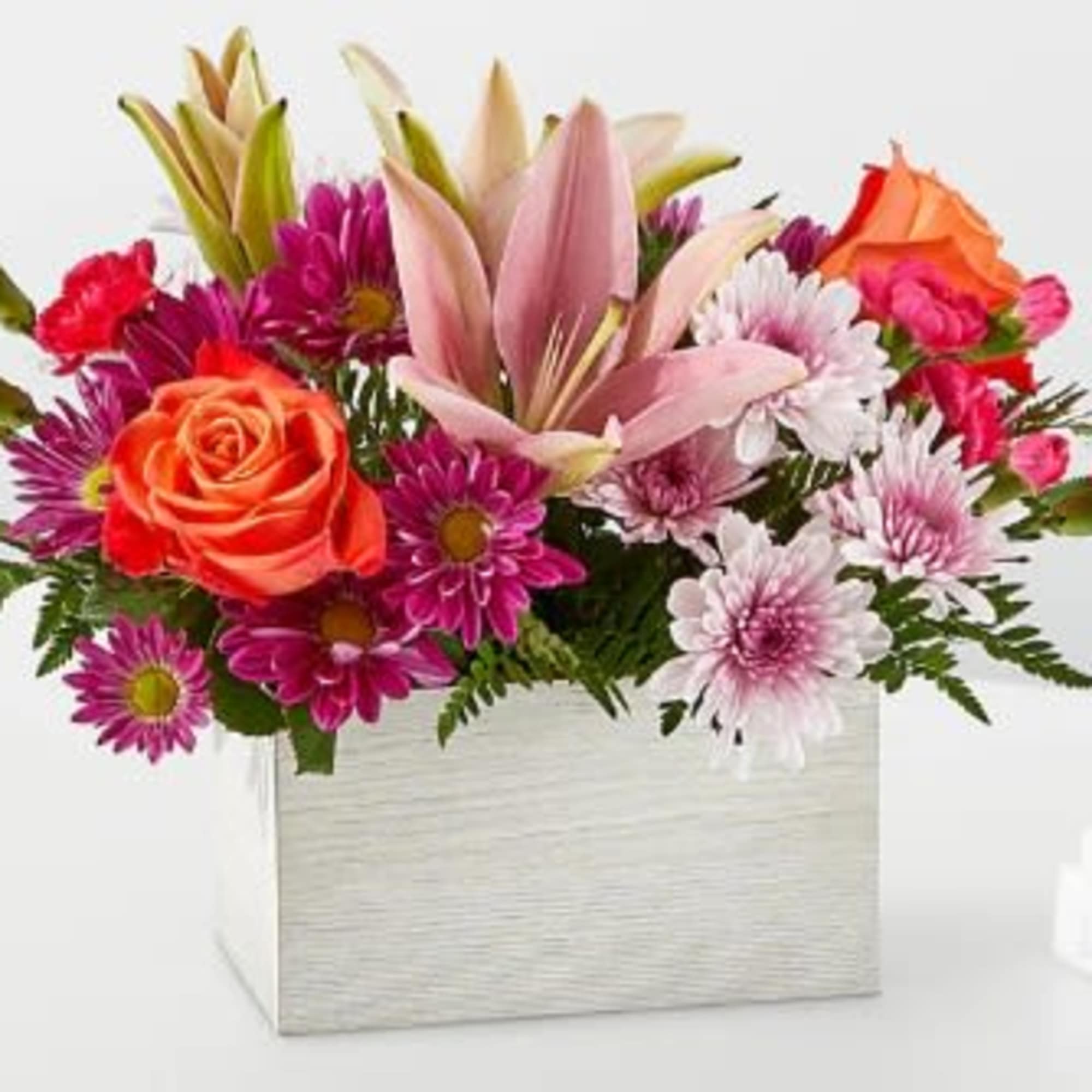 Rectangular arrangement of pink lilies, orange roses, and purple and white daisies in a white box.