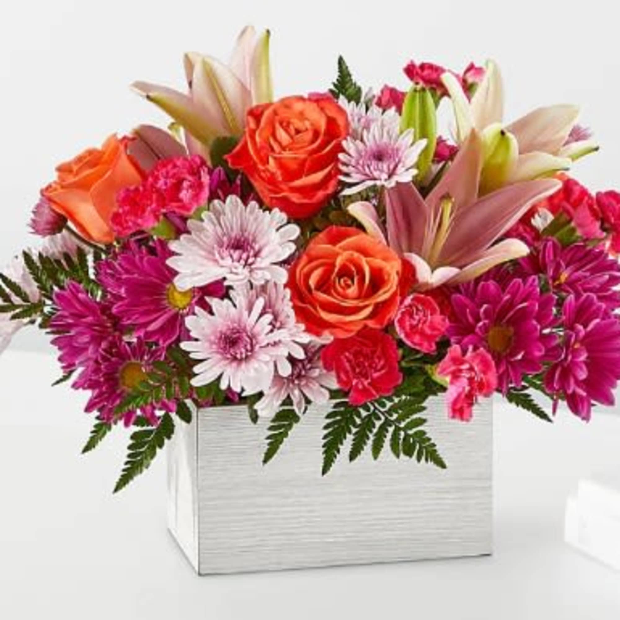 Bright arrangement of orange roses, pink lilies, carnations, and mums in a white rectangular container