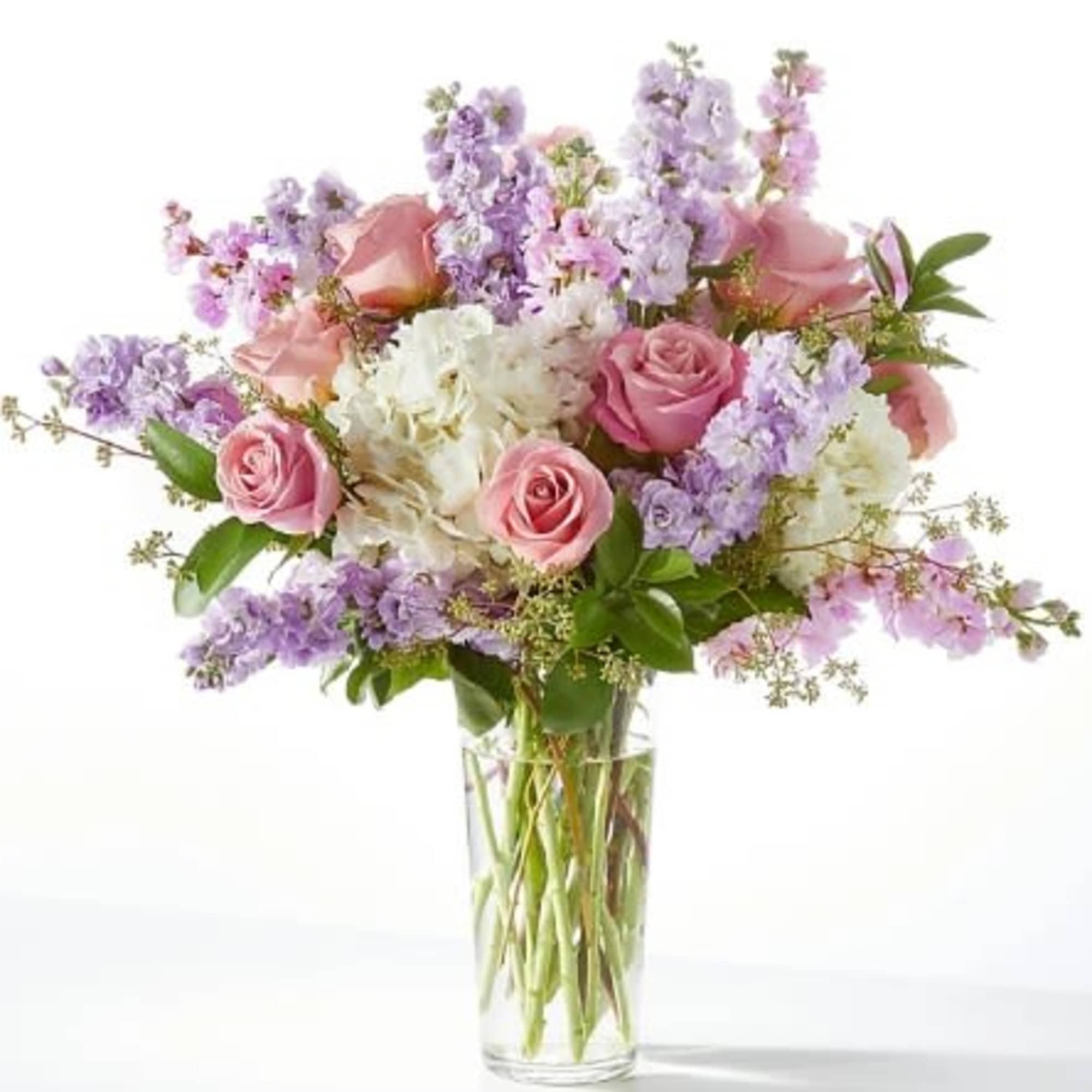 Tall arrangement of pink roses, white hydrangea, and lavender stock in a clear glass vase