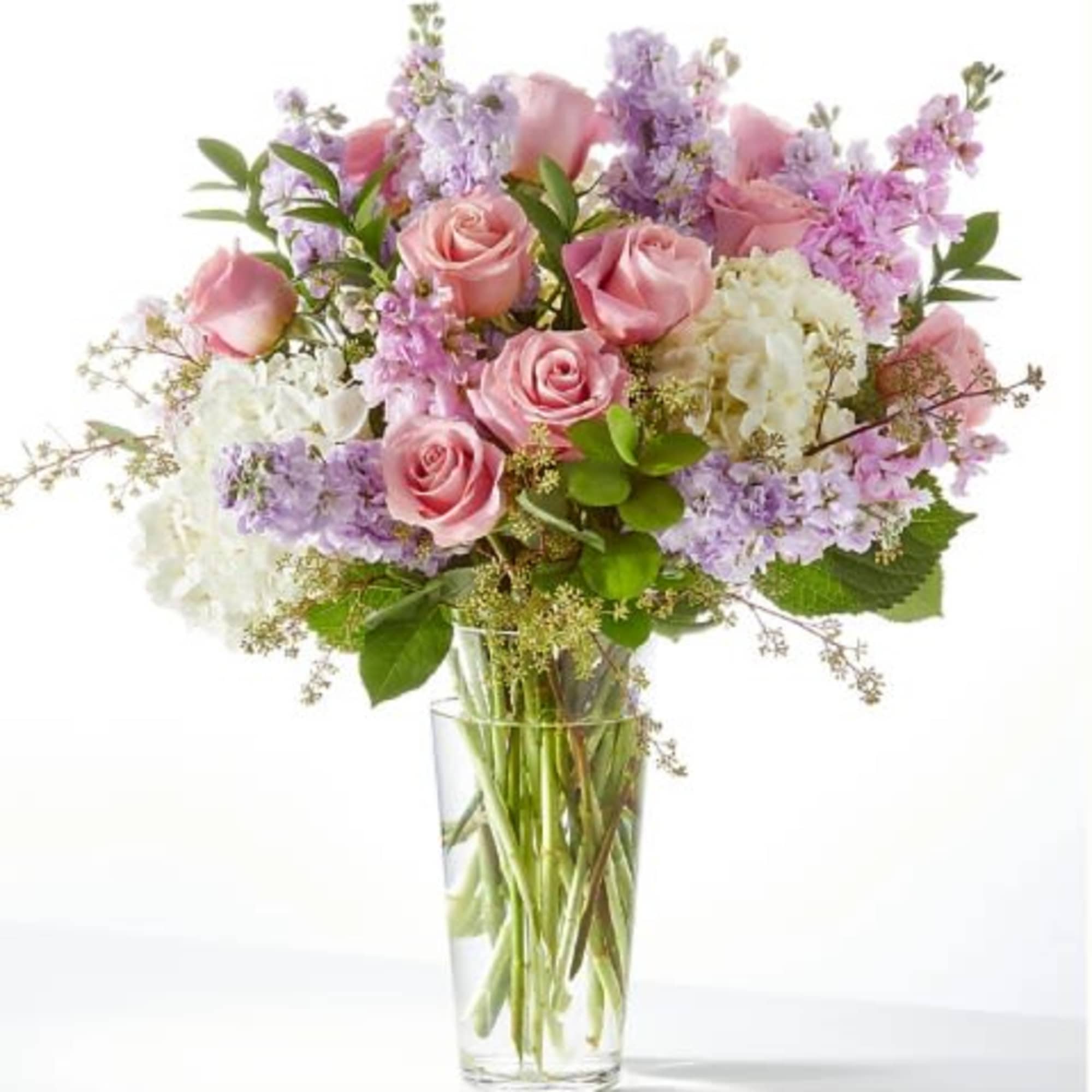 Tall glass vase of pink roses, lavender stock, and white hydrangeas in a mixed bouquet