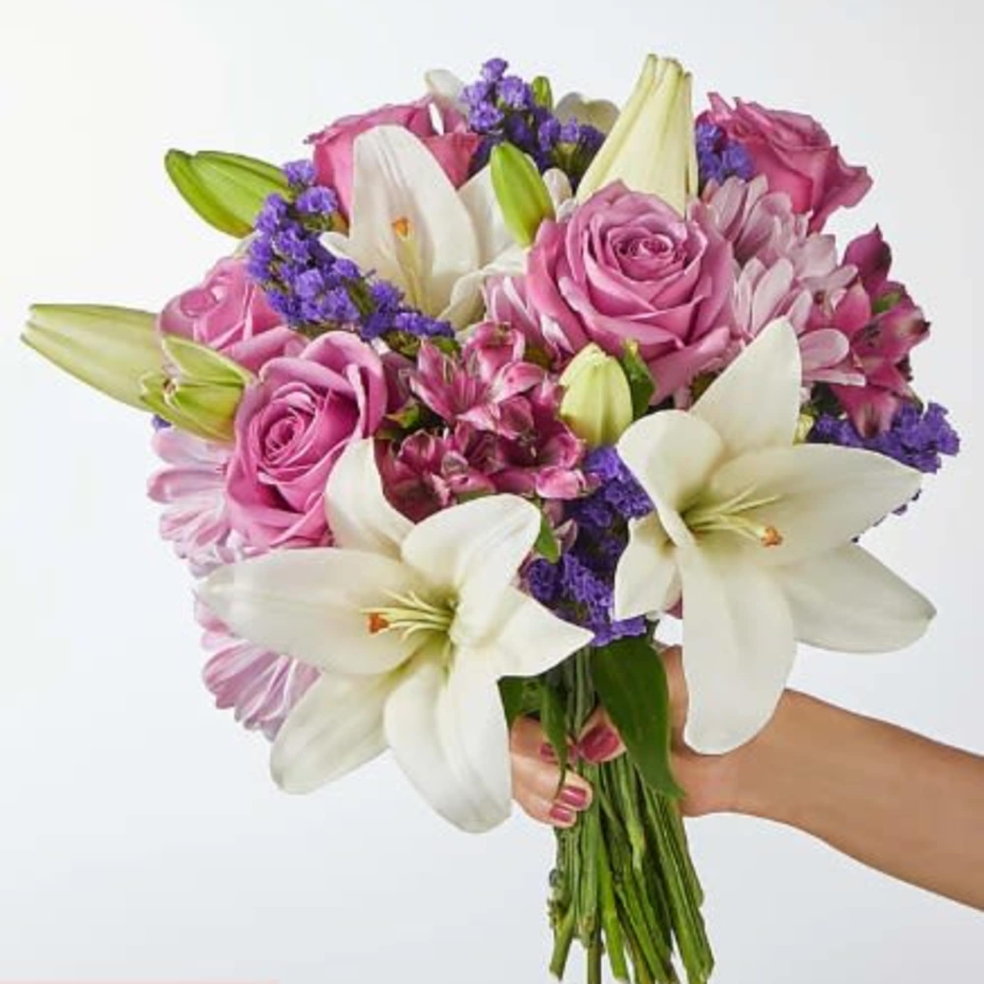 Hand-tied bouquet of white lilies, pink roses, and purple filler flowers held against a light background