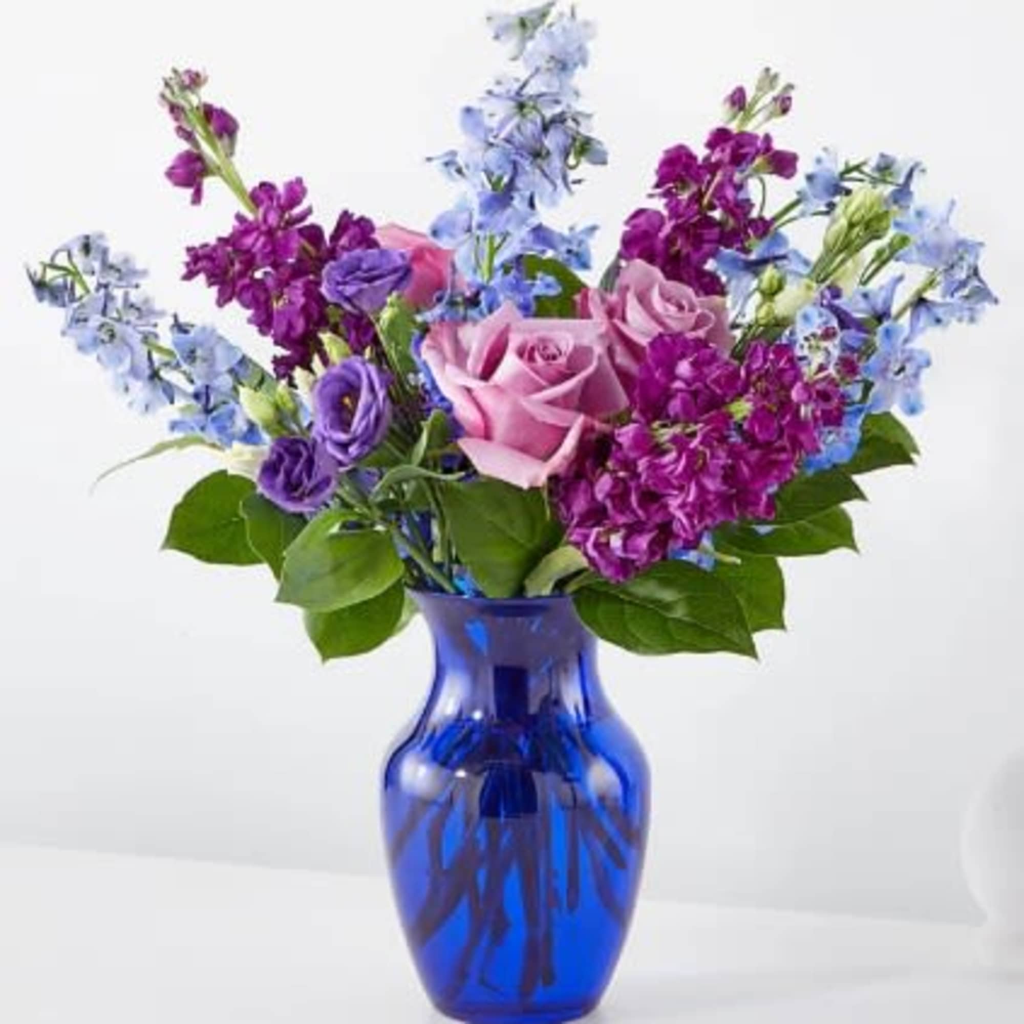 Mixed bouquet of pink roses and purple flowers in a cobalt blue glass vase