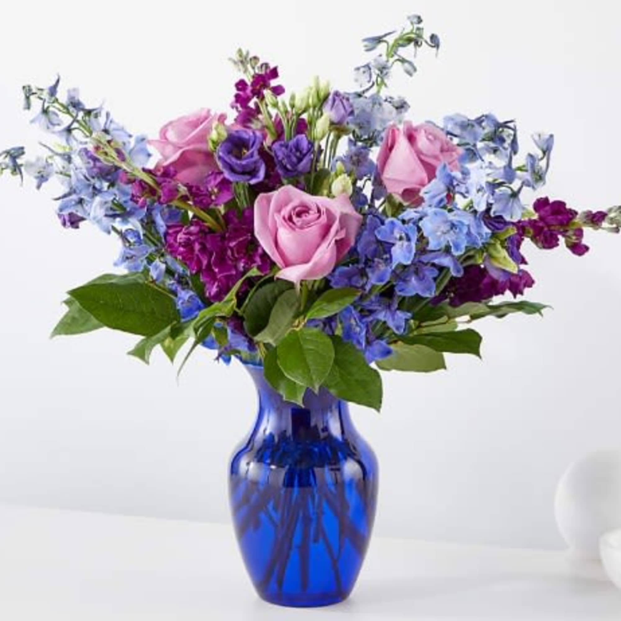 Mixed bouquet of pink roses with purple and blue flowers in a bright blue glass vase