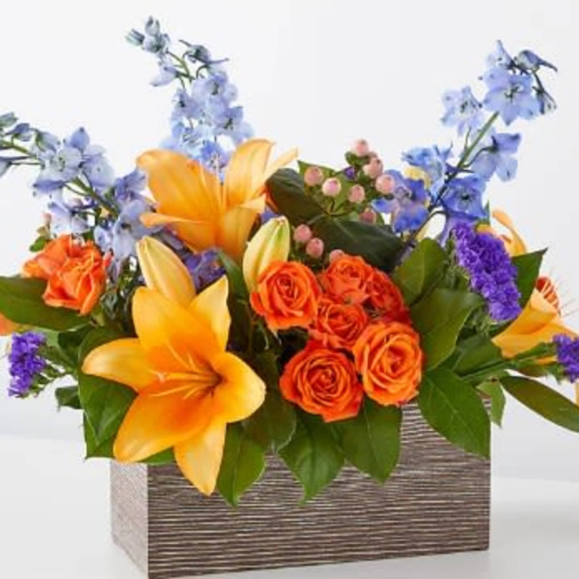 Mixed bouquet of orange roses, yellow lilies, and blue flowers in a rectangular box