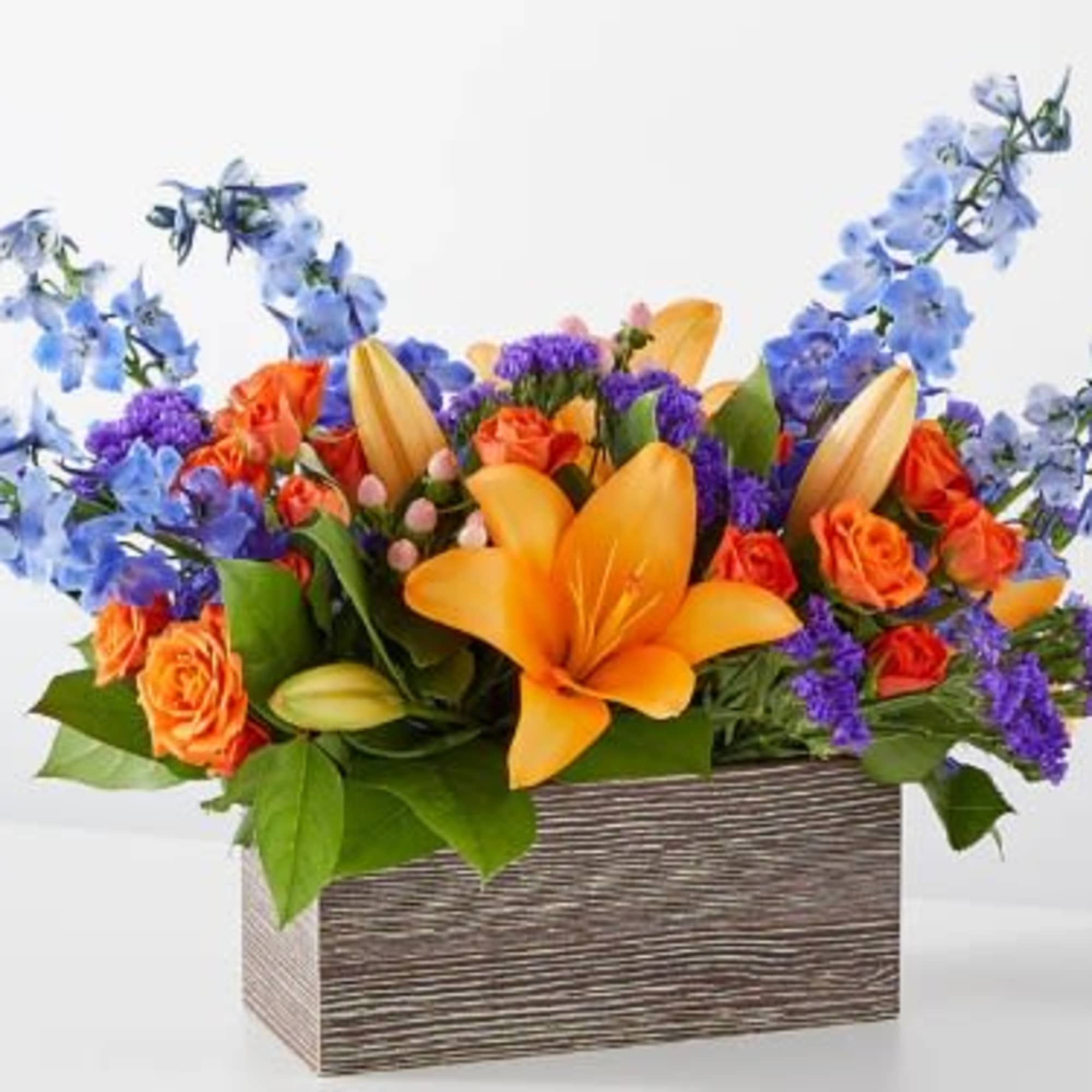 Orange lilies and roses in a rectangular wood-look container with blue flowers