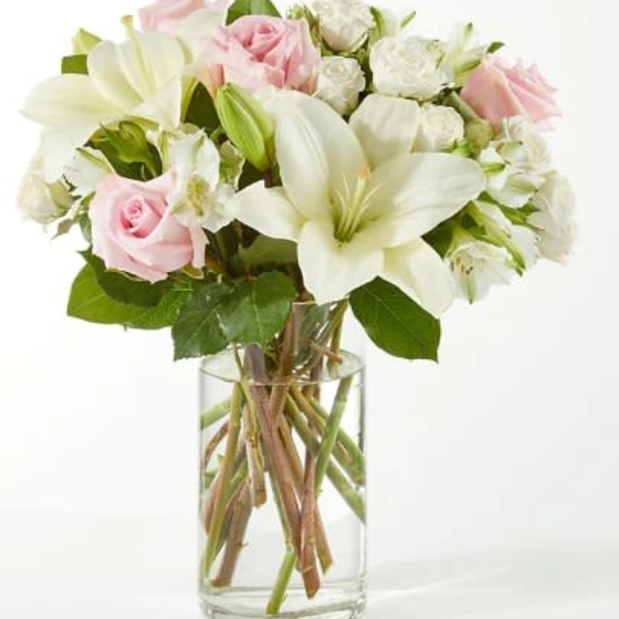 Arrangement of white lilies and white and pink roses in a clear glass cylinder vase