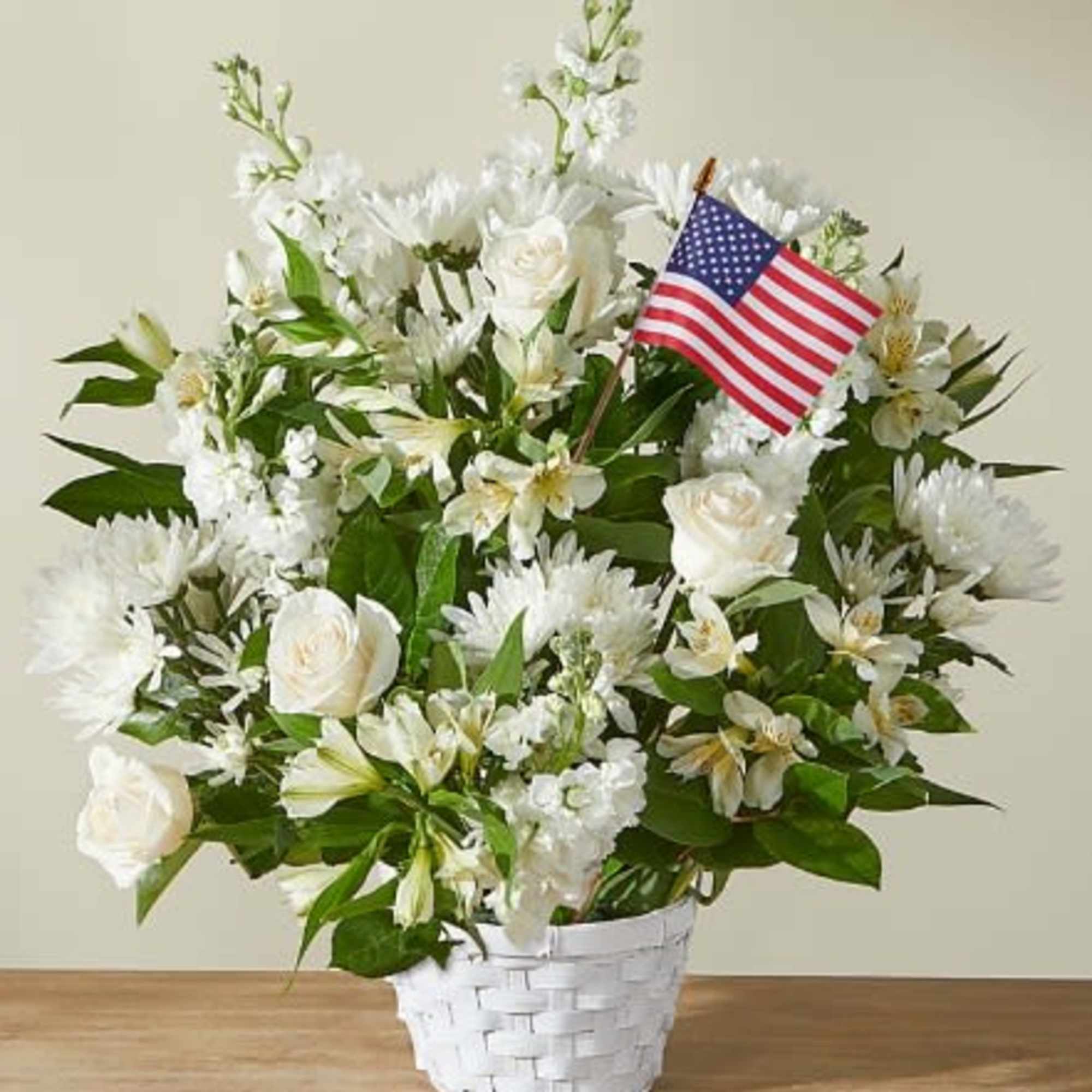 White floral arrangement in a white basket with a small American flag