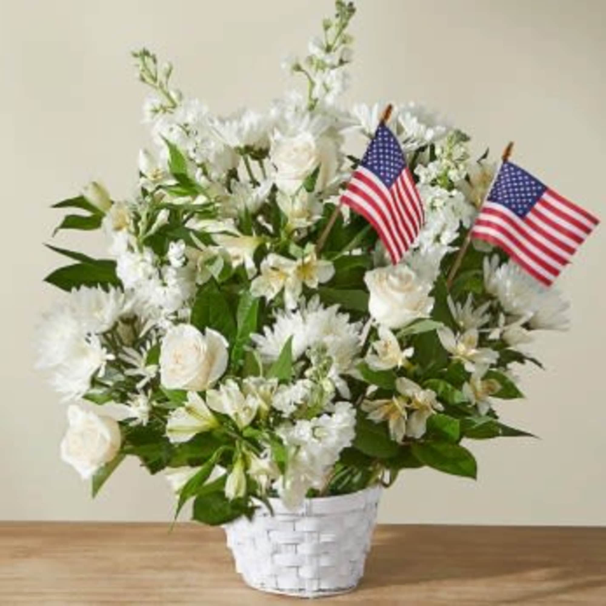 White floral arrangement in a white basket with two small American flags