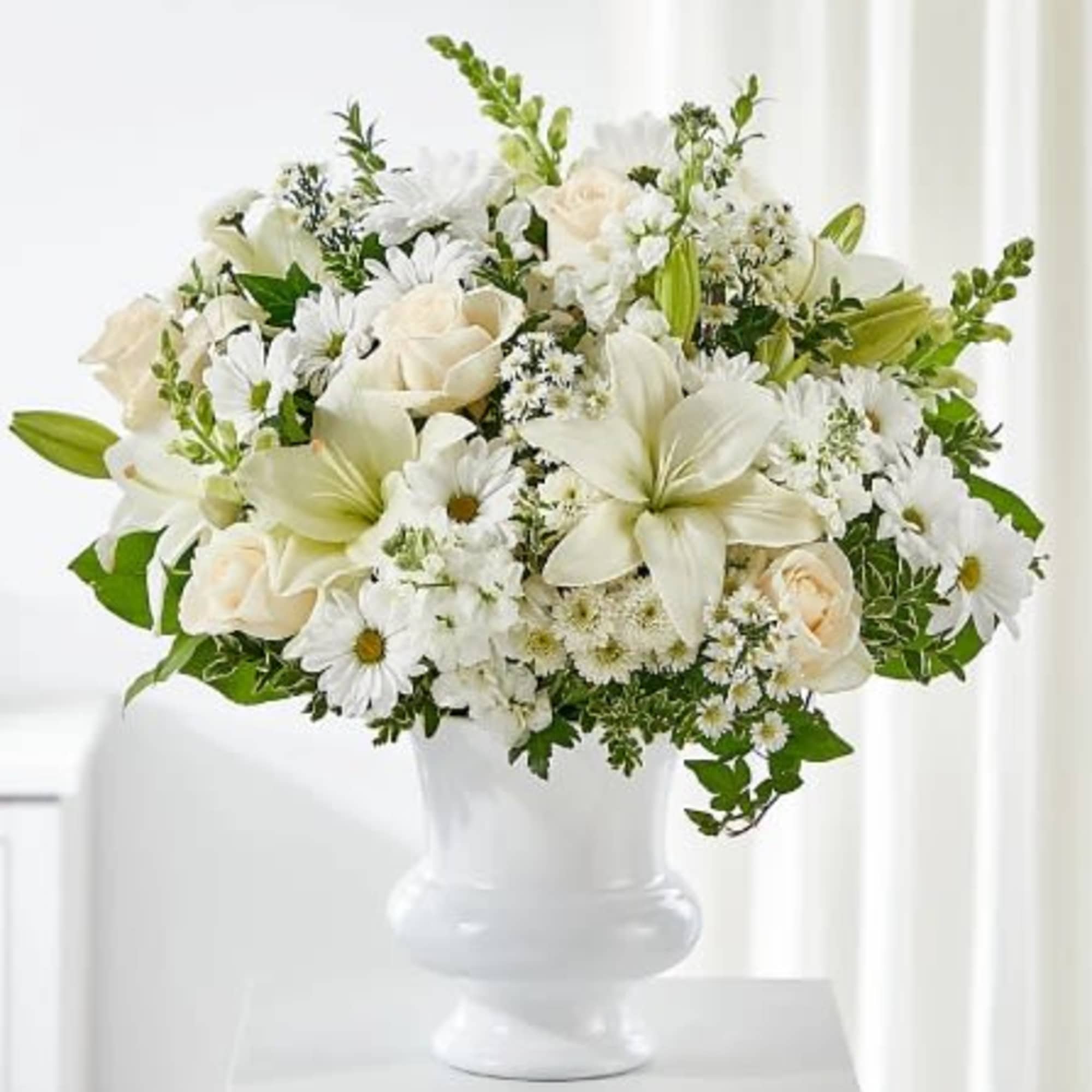 White floral arrangement in a white vase with roses, lilies, and daisies