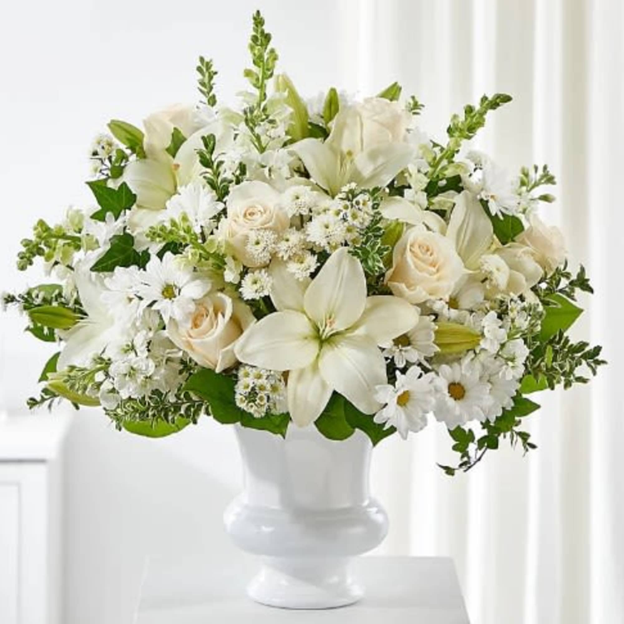 White floral arrangement in a white vase with roses and lilies