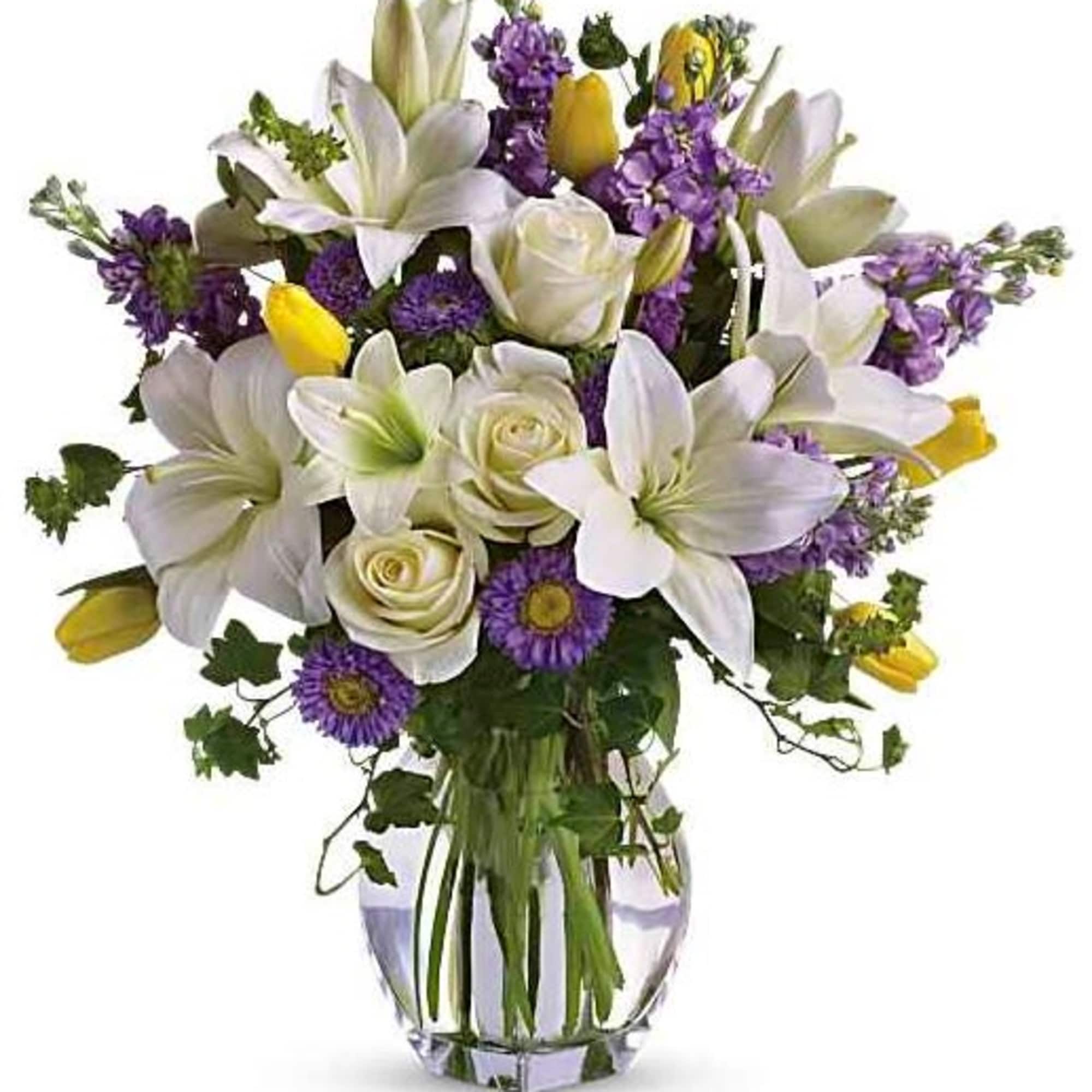 White lilies, roses, and purple flowers in a clear glass vase