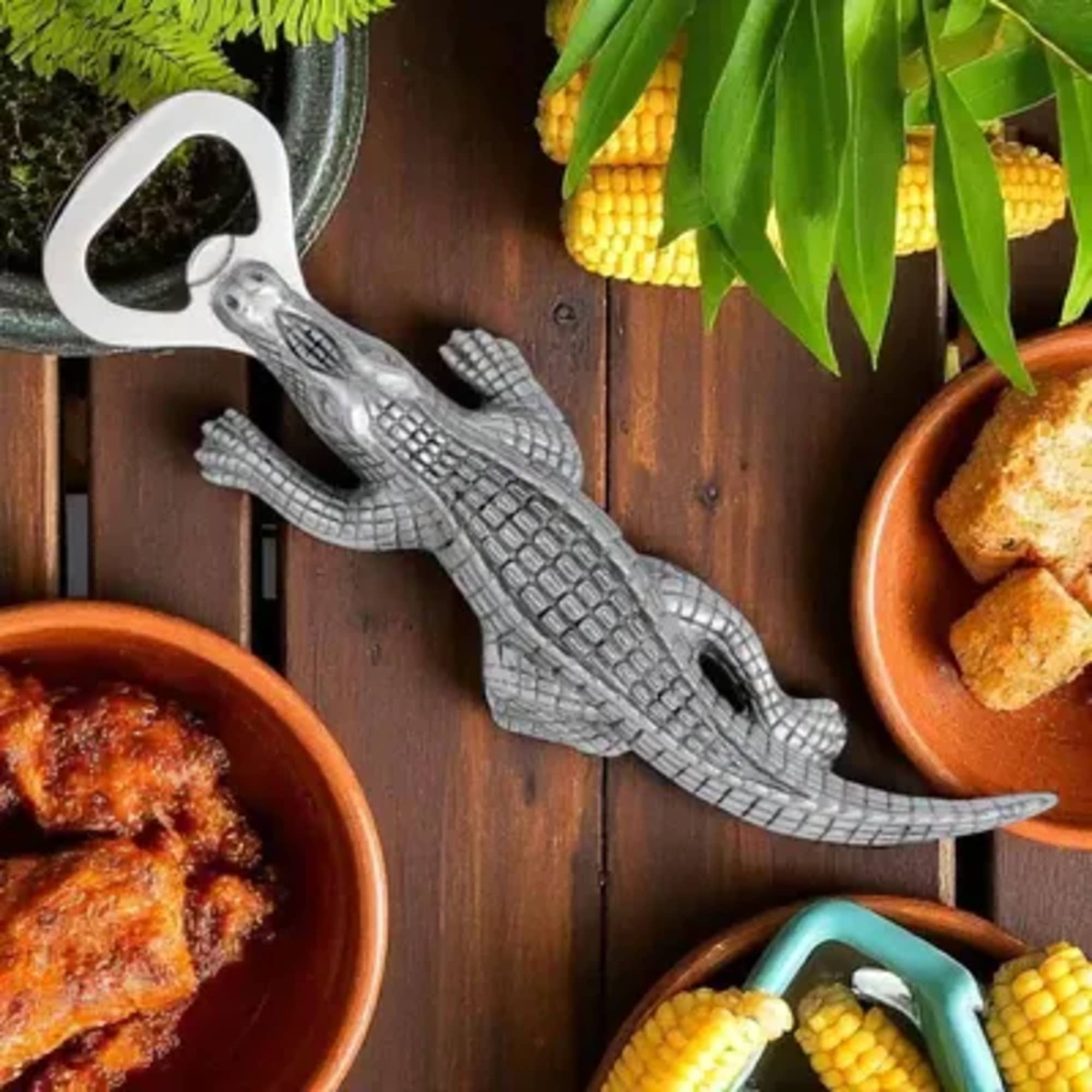 Gray crocodile bottle opener on a wooden table with bowls of food.