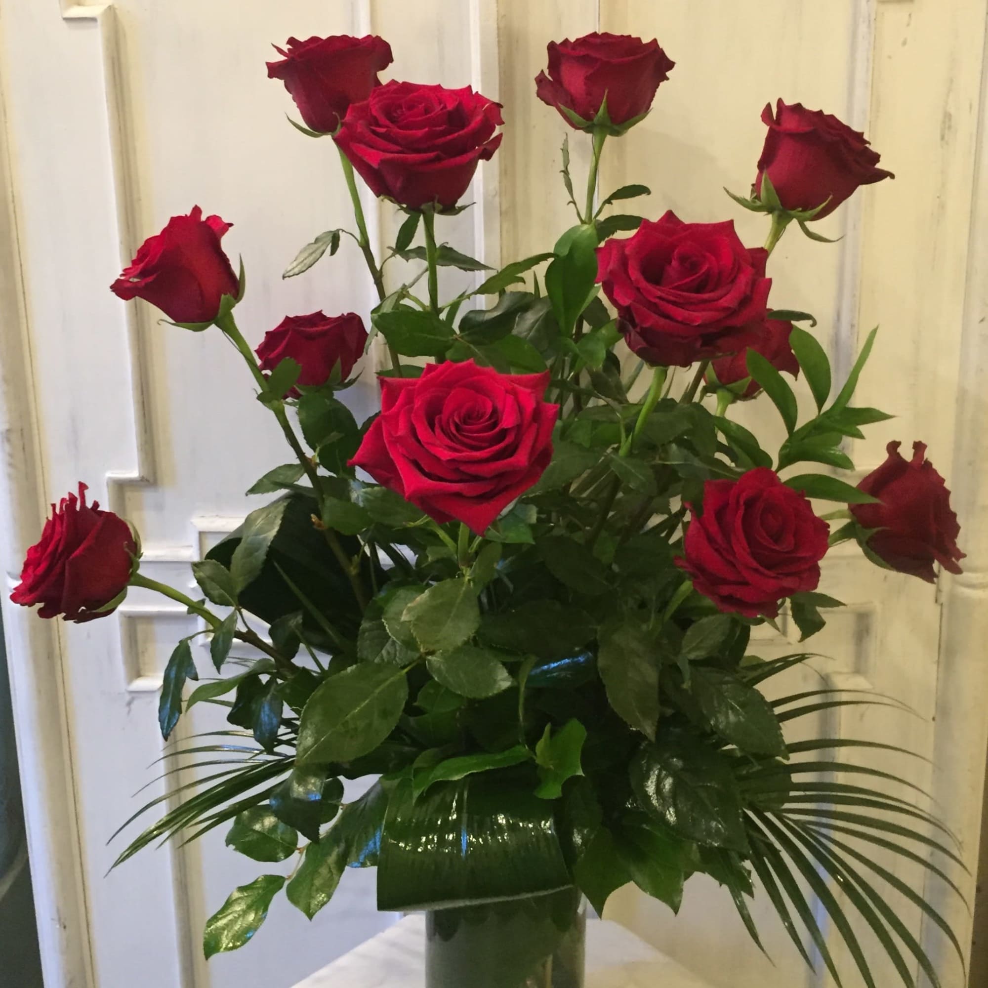 Red roses arranged in a clear glass vase with greenery