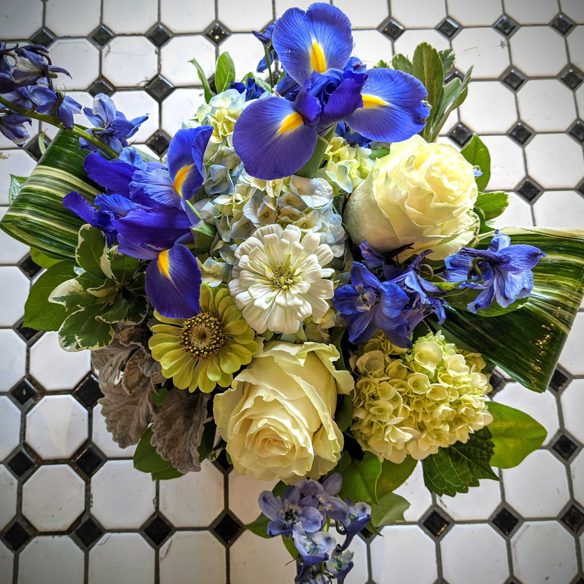 Compact arrangement of blue irises, white roses, hydrangeas and mixed blooms in a round design