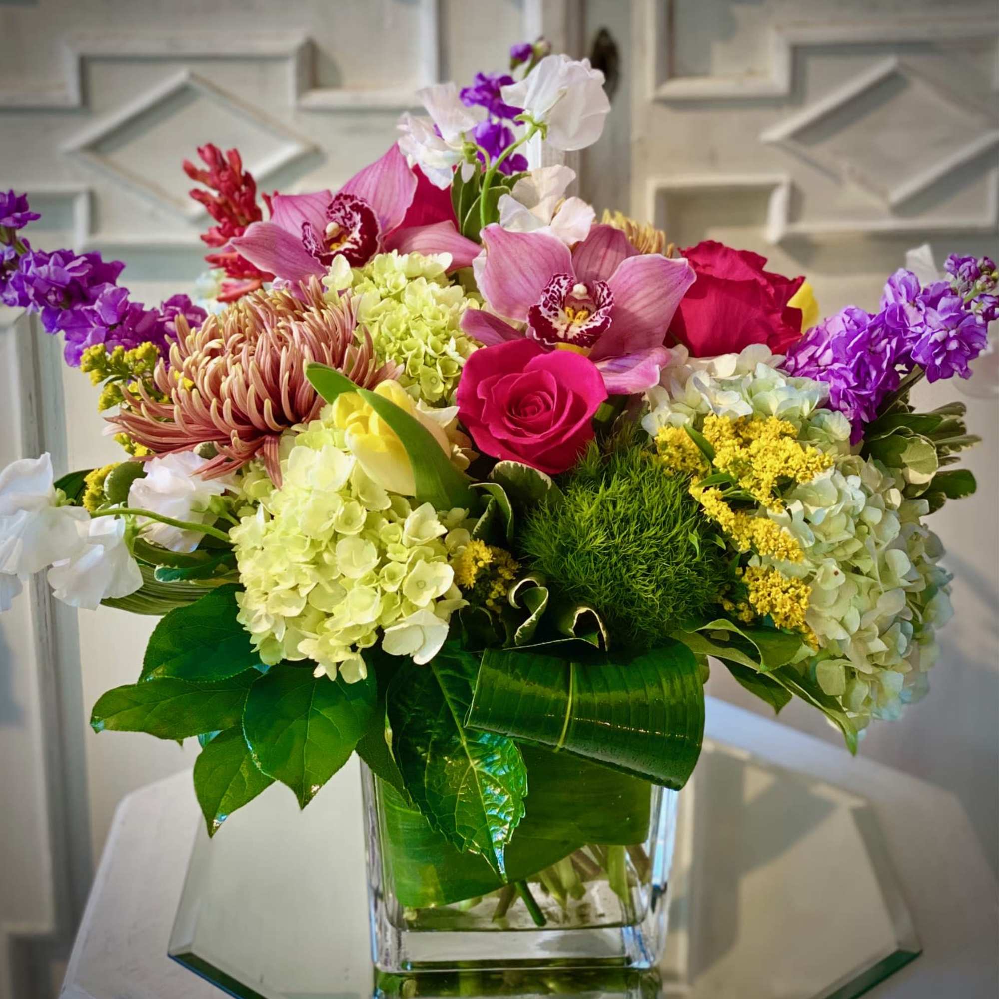 Colorful mixed bouquet in a clear glass vase with roses and orchids