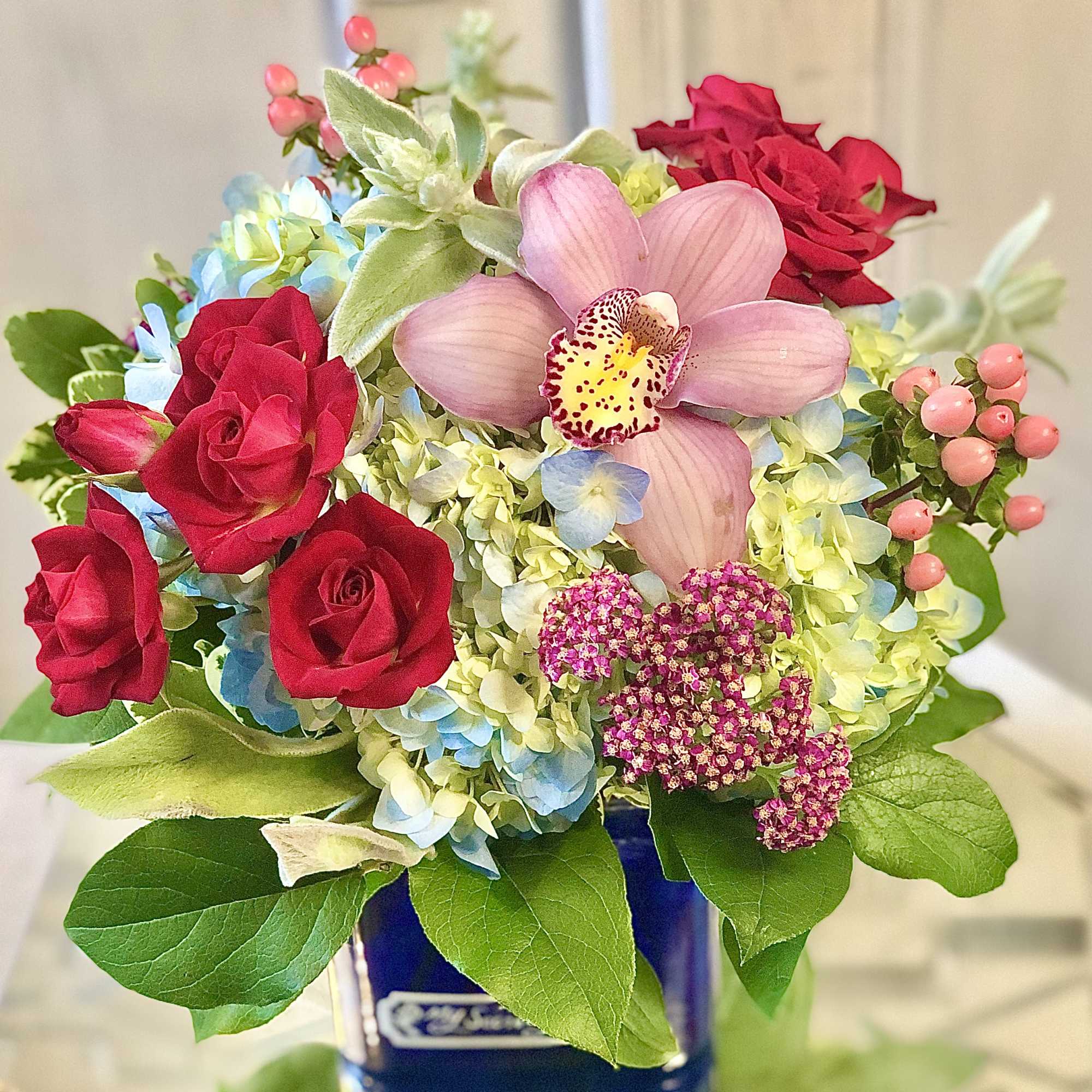 Bouquet of red roses, pink orchid, and blue hydrangea in a blue vase